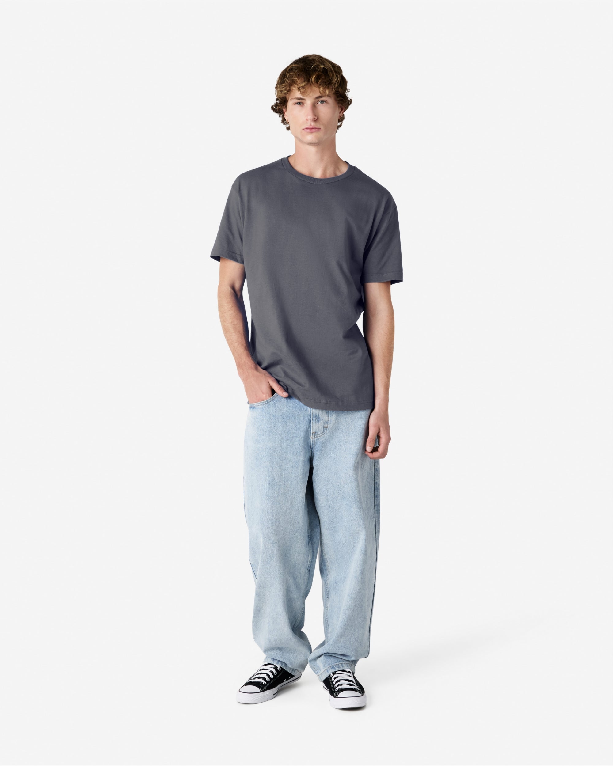 Male Model wearing a Charcoal Heavyweight Unisex Short Sleeve Crew Neck Tee, paired with blue jeans, standing against a plain background (front pose) -charcoal