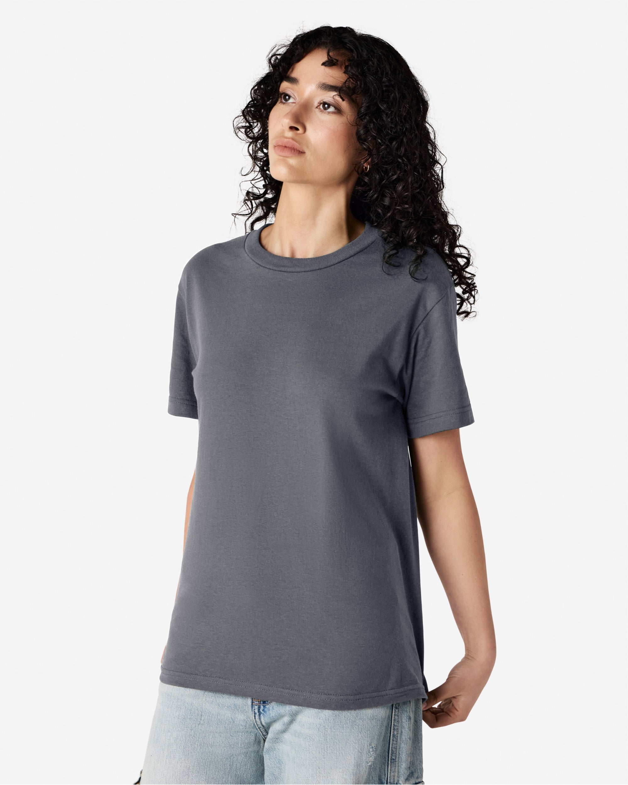 Female Model wearing a Charcoal Heavyweight Unisex Short Sleeve Crew Neck Tee, paired with blue jeans, standing against a plain background (front pose) -charcoal