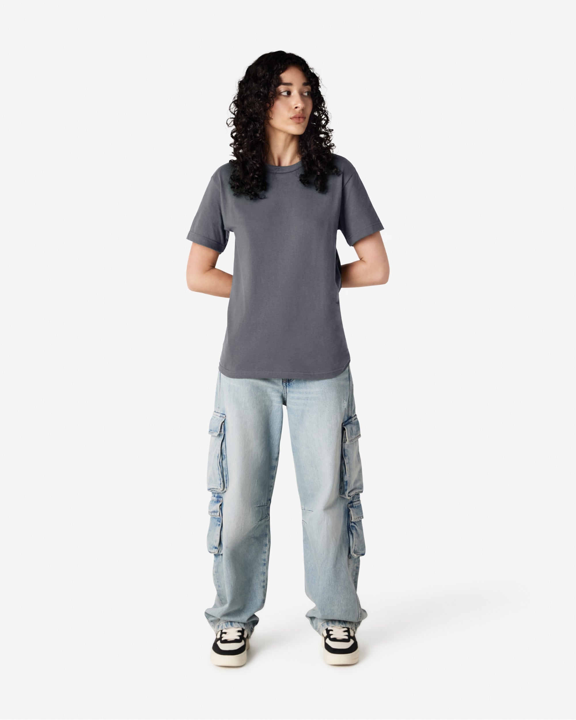 Female Model wearing a Charcoal Heavyweight Unisex Short Sleeve Crew Neck Tee, paired with blue jeans, standing against a plain background (front pose) -charcoal