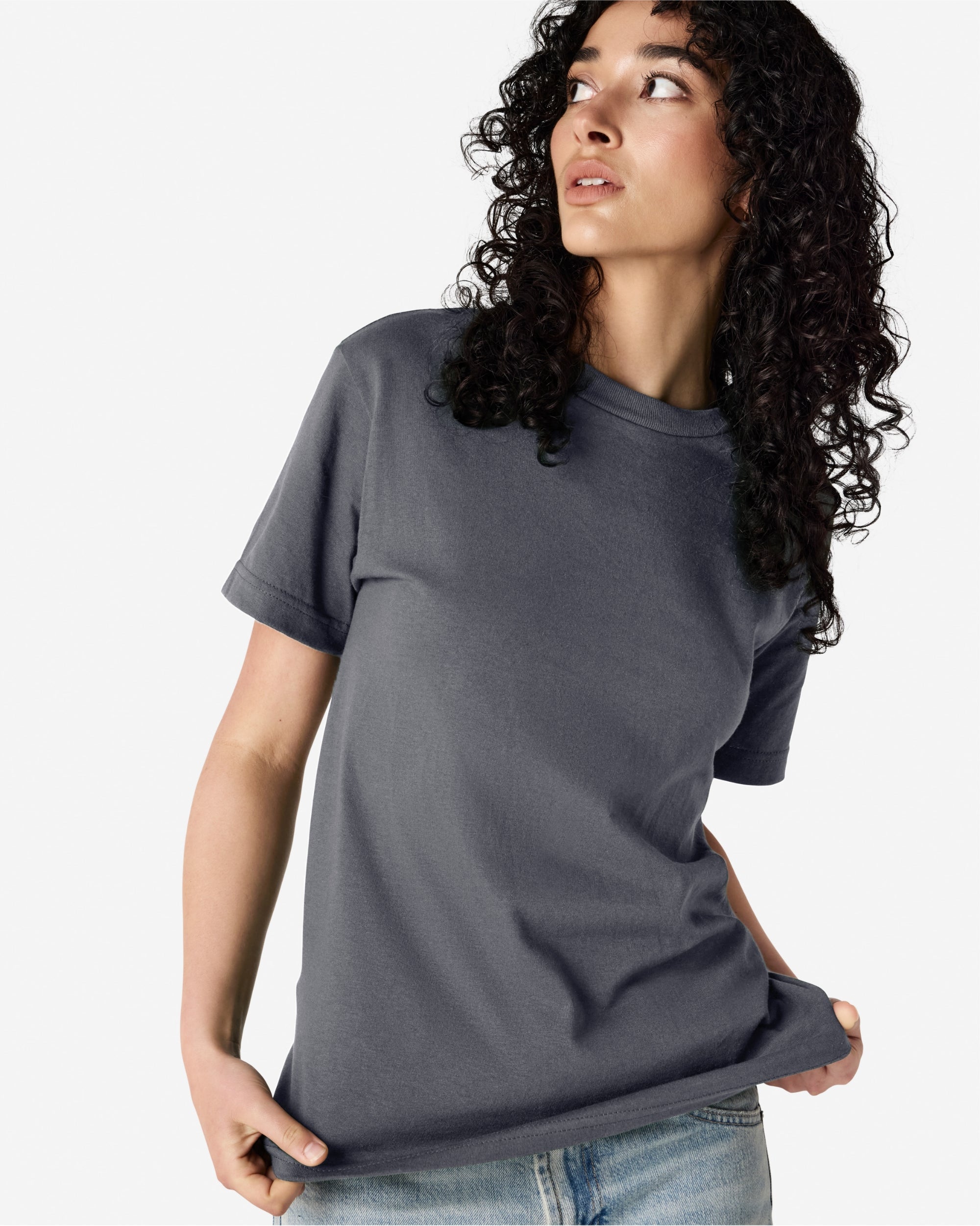 Female Model wearing a Charcoal Heavyweight Unisex Short Sleeve Crew Neck Tee, paired with blue jeans, standing against a plain background (front pose) -charcoal