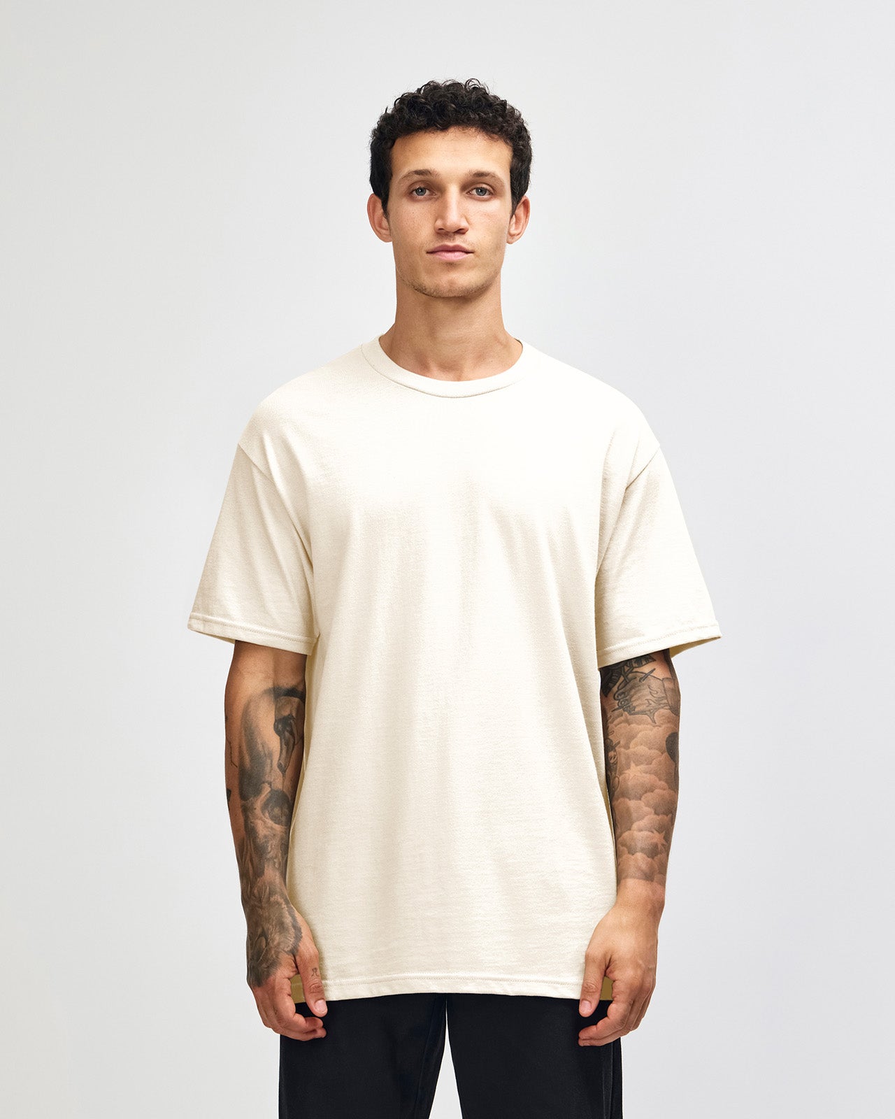 Male Model wearing a Charcoal Heavyweight Unisex Short Sleeve Crew Neck Tee, paired with blue jeans, standing against a plain background (front pose) -cream