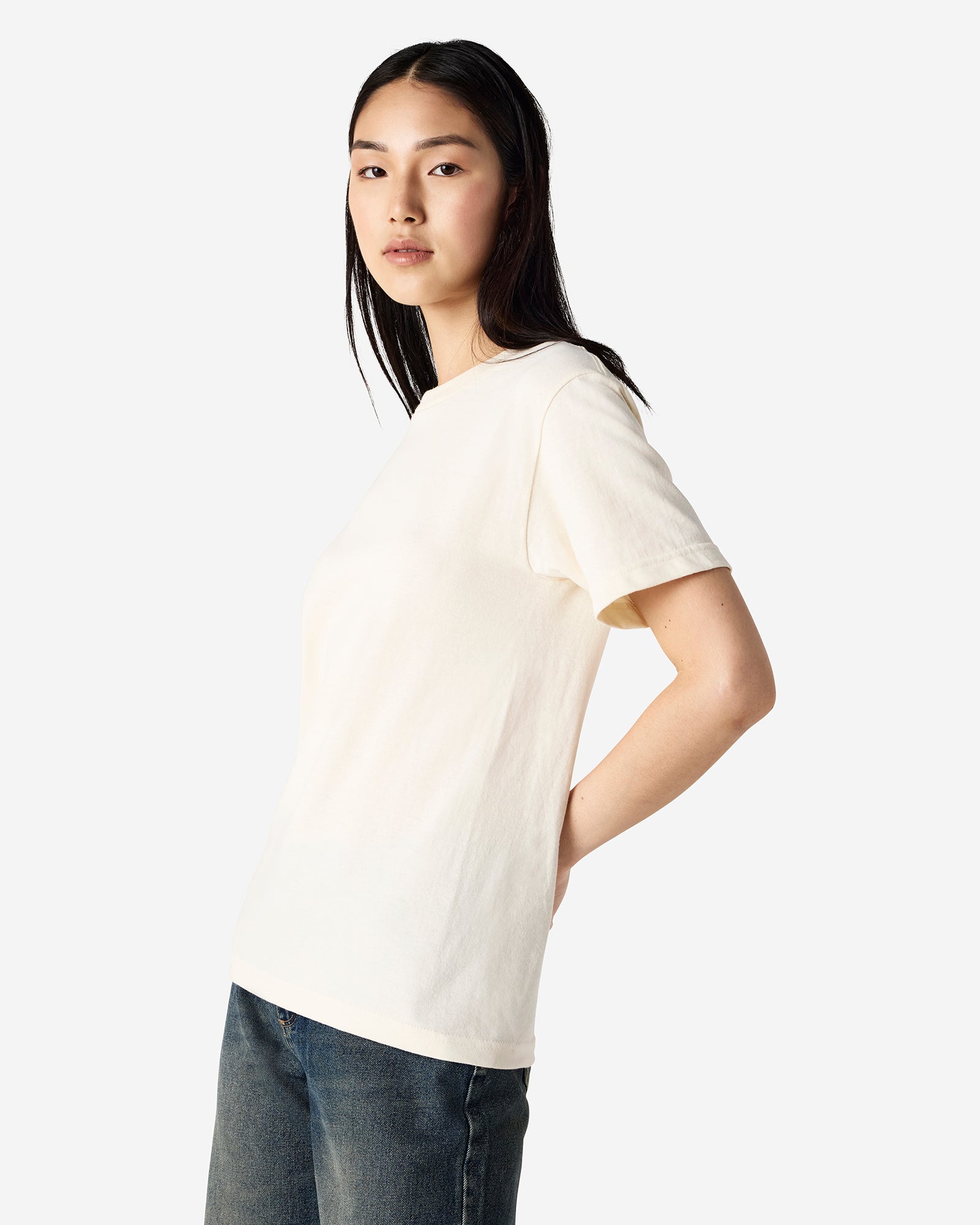 Female Model wearing a Cream Heavyweight Unisex Short Sleeve Crew Neck Tee, paired with blue jeans, standing against a plain background (front pose) -cream
