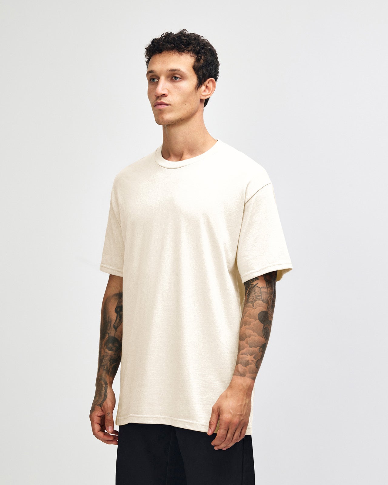 Male Model wearing a Charcoal Heavyweight Unisex Short Sleeve Crew Neck Tee, paired with blue jeans, standing against a plain background (front pose) -cream