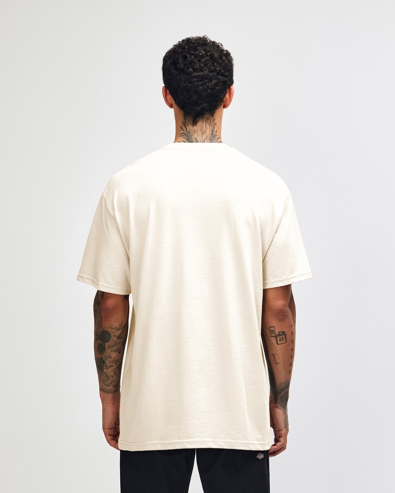 Male Model wearing a Charcoal Heavyweight Unisex Short Sleeve Crew Neck Tee, paired with blue jeans, standing against a plain background (front pose) -cream