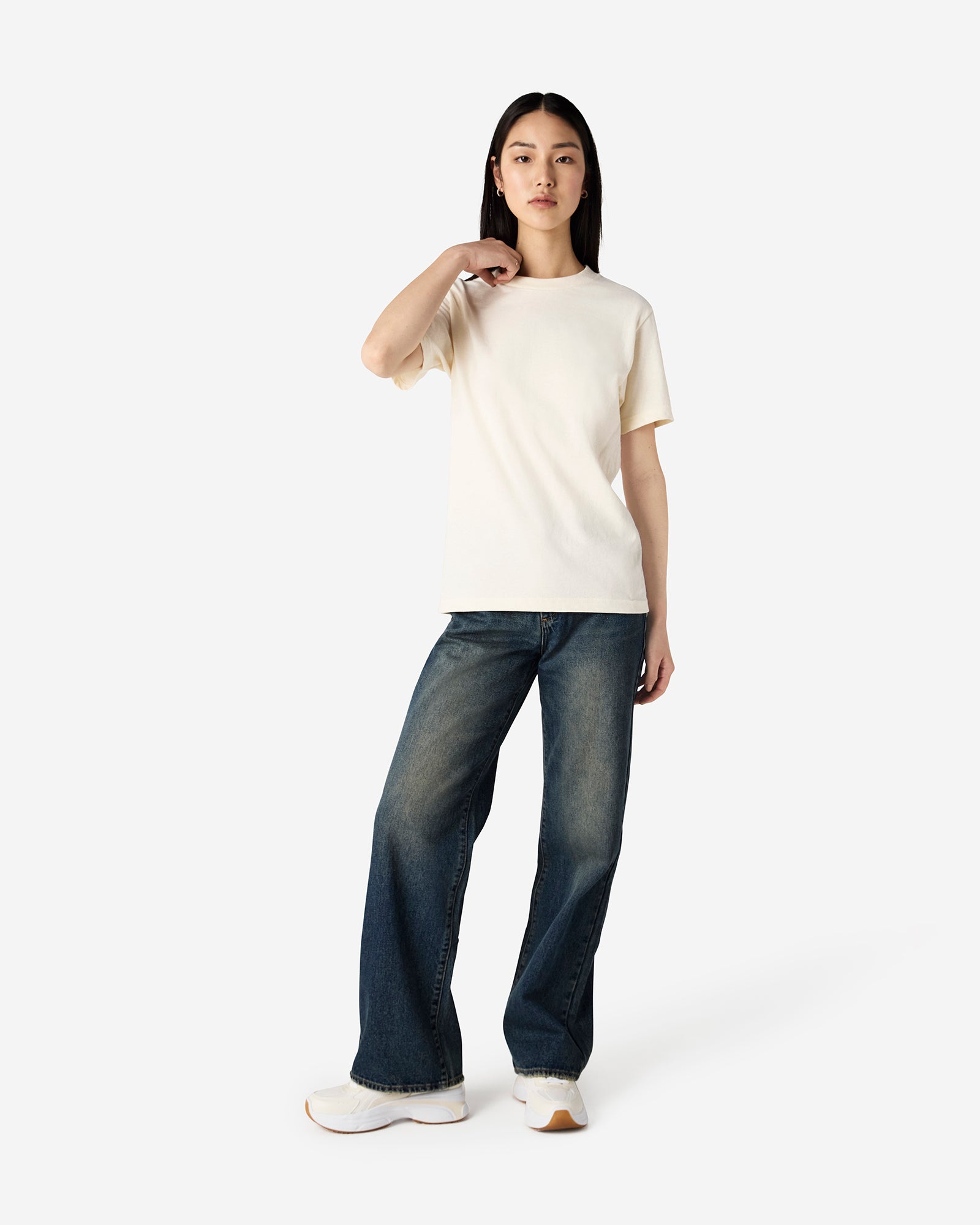 Female Model wearing a Cream Heavyweight Unisex Short Sleeve Crew Neck Tee, paired with blue jeans, standing against a plain background (front pose) -cream