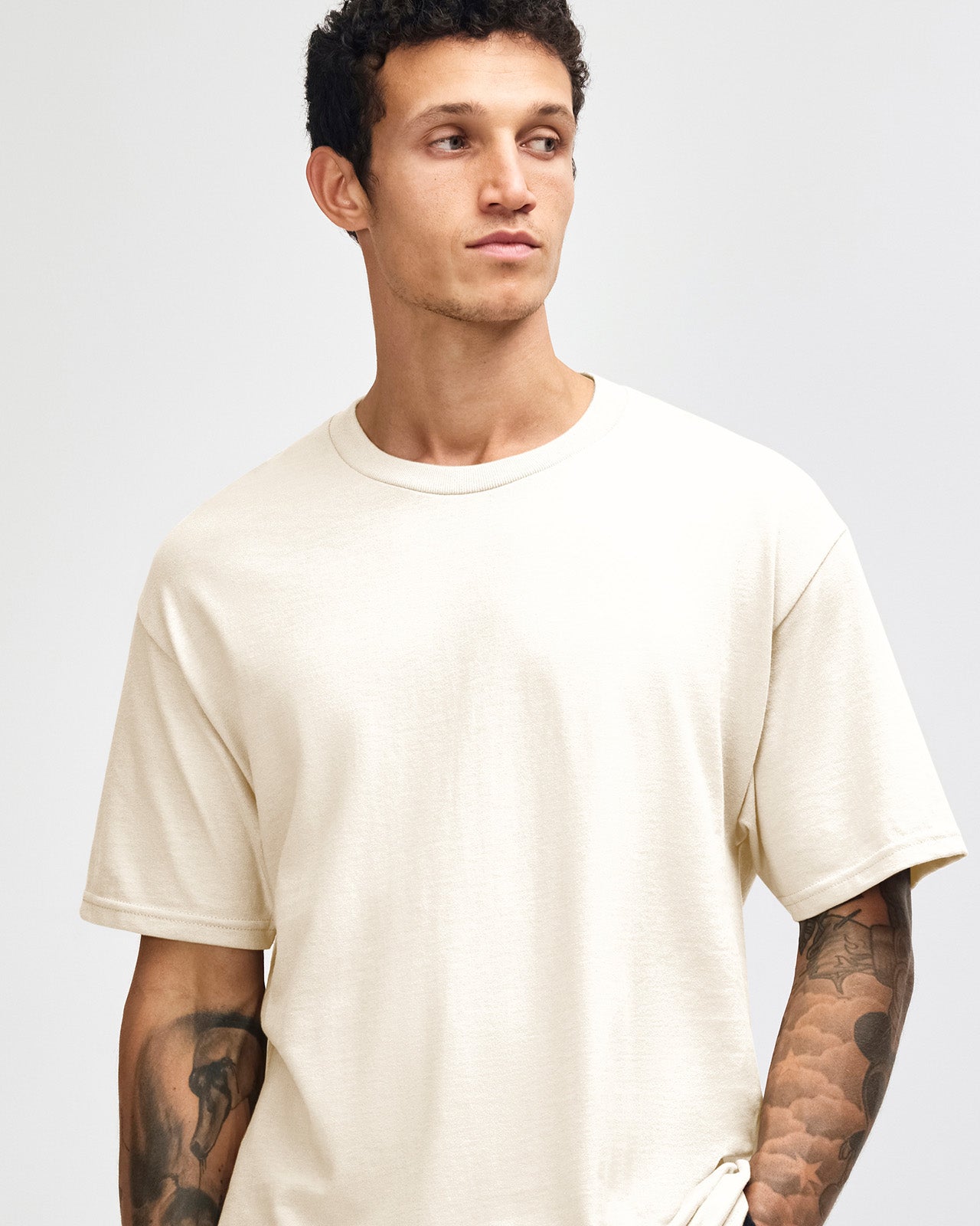Male Model wearing a Charcoal Heavyweight Unisex Short Sleeve Crew Neck Tee, paired with blue jeans, standing against a plain background (front pose) -cream