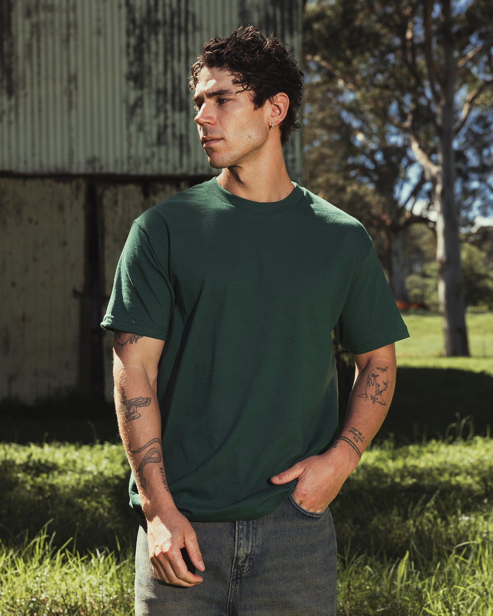 image of Unisex Heavy T-shirt : Male Model wearing a Forest Heavyweight Unisex Short Sleeve Crew Neck Tee, paired with blue jeans, standing against a plain background (front pose) -forest green