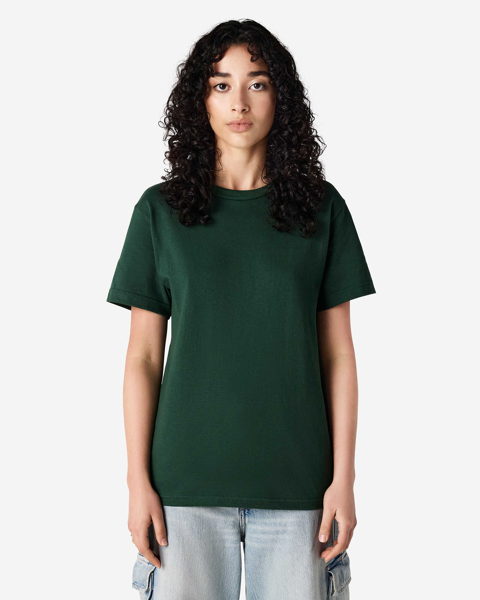 Female Model wearing a Forest Heavyweight Unisex Short Sleeve Crew Neck Tee, paired with blue jeans, standing against a plain background (front pose) -forest green