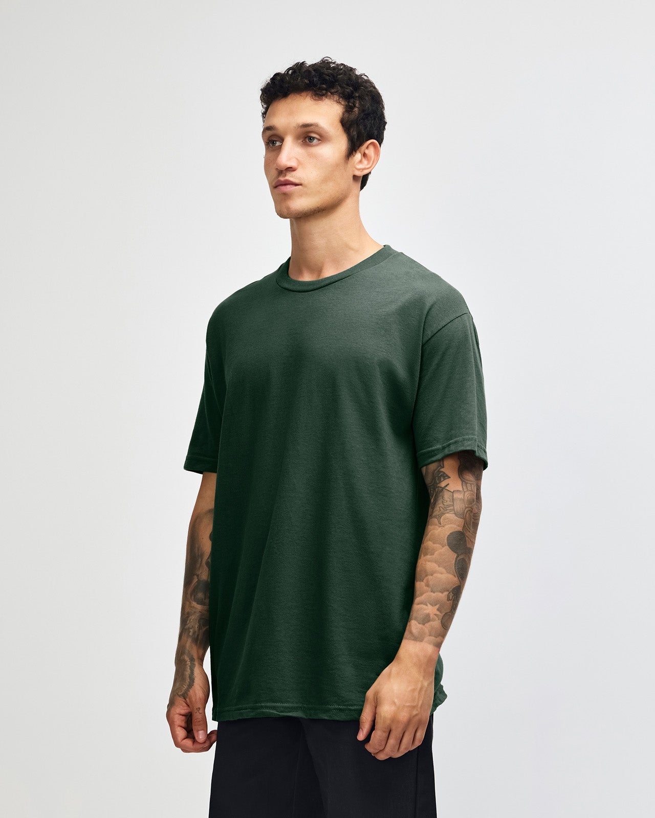 Male Model wearing a Forest Heavyweight Unisex Short Sleeve Crew Neck Tee, paired with blue jeans, standing against a plain background (front pose) -forest green