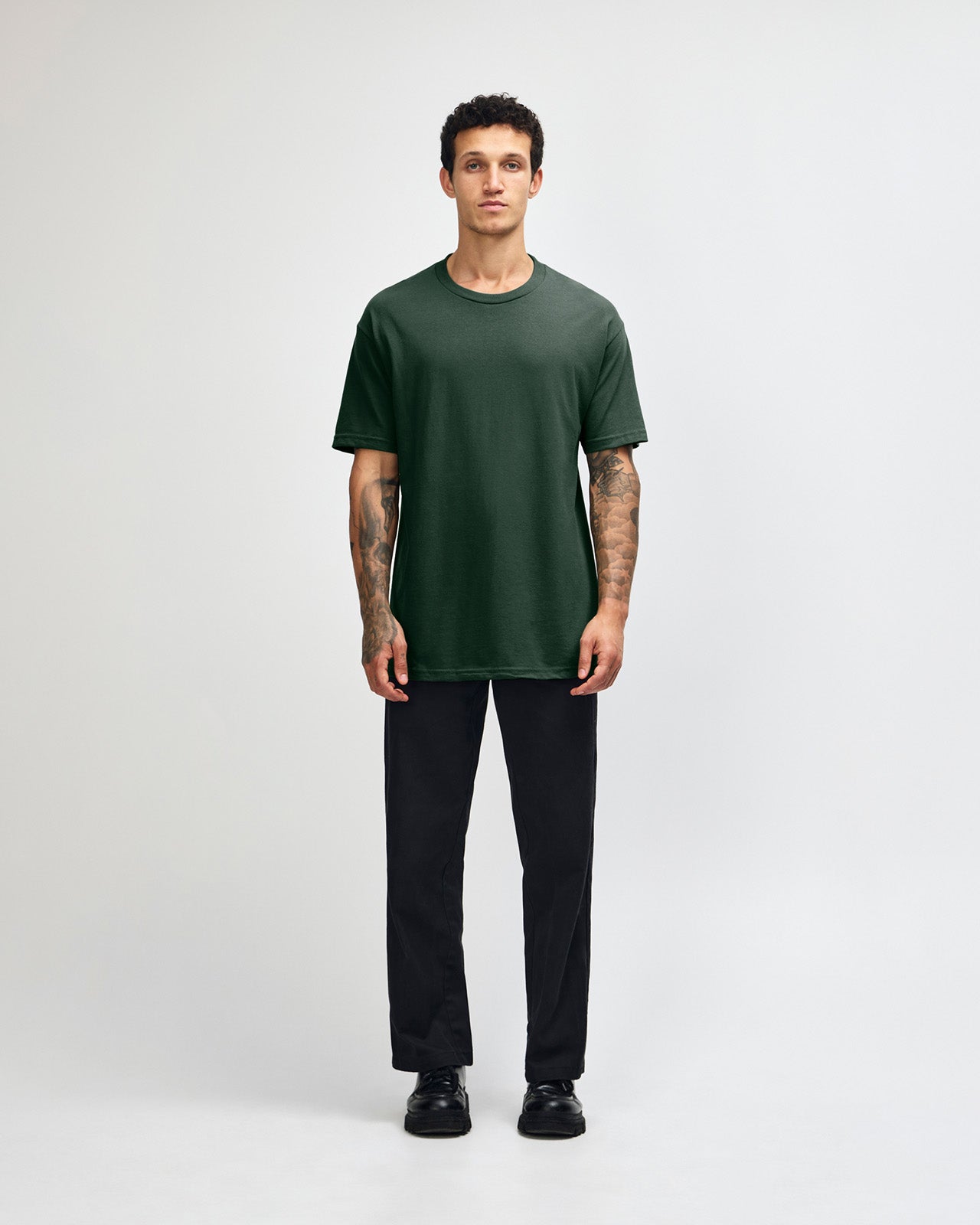Male Model wearing a Forest Heavyweight Unisex Short Sleeve Crew Neck Tee, paired with blue jeans, standing against a plain background (front pose) -forest green