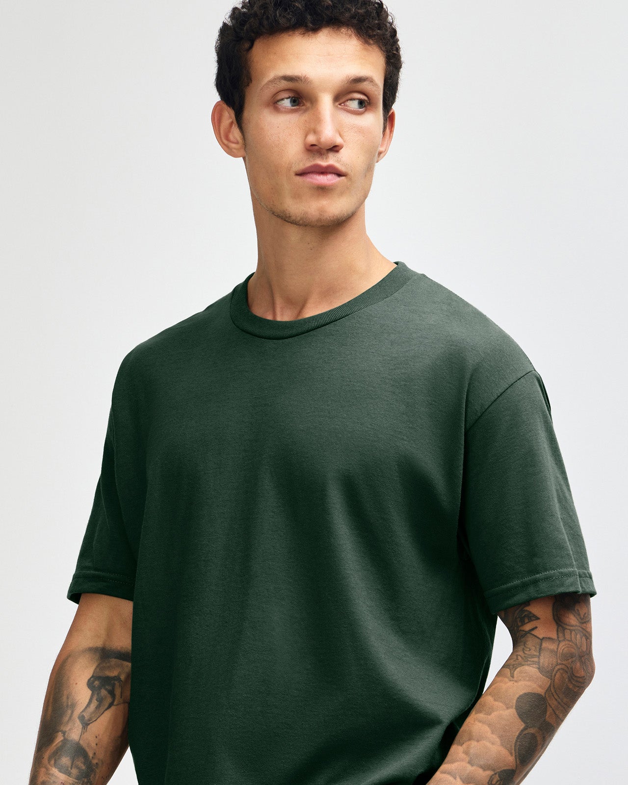 Male Model wearing a Forest Heavyweight Unisex Short Sleeve Crew Neck Tee, paired with blue jeans, standing against a plain background (front pose) -forest green