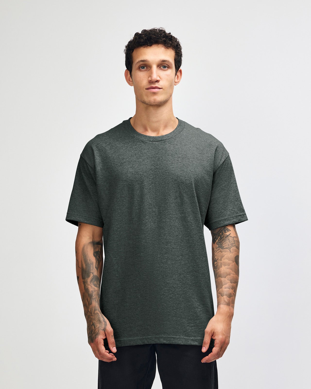 Male Model wearing a Heather Charcoal Heavyweight Unisex Short Sleeve Crew Neck Tee, paired with blue jeans, standing against a plain background (front pose) -heather charcoal
