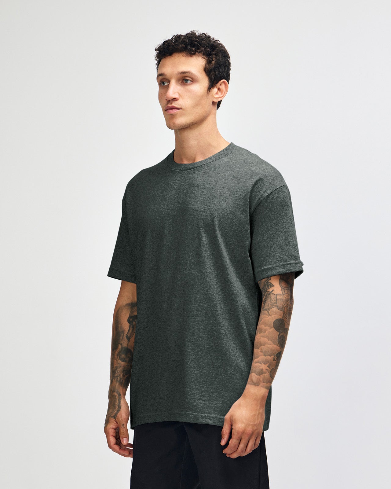 Male Model wearing a Heather Charcoal Heavyweight Unisex Short Sleeve Crew Neck Tee, paired with blue jeans, standing against a plain background (front pose) -heather charcoal