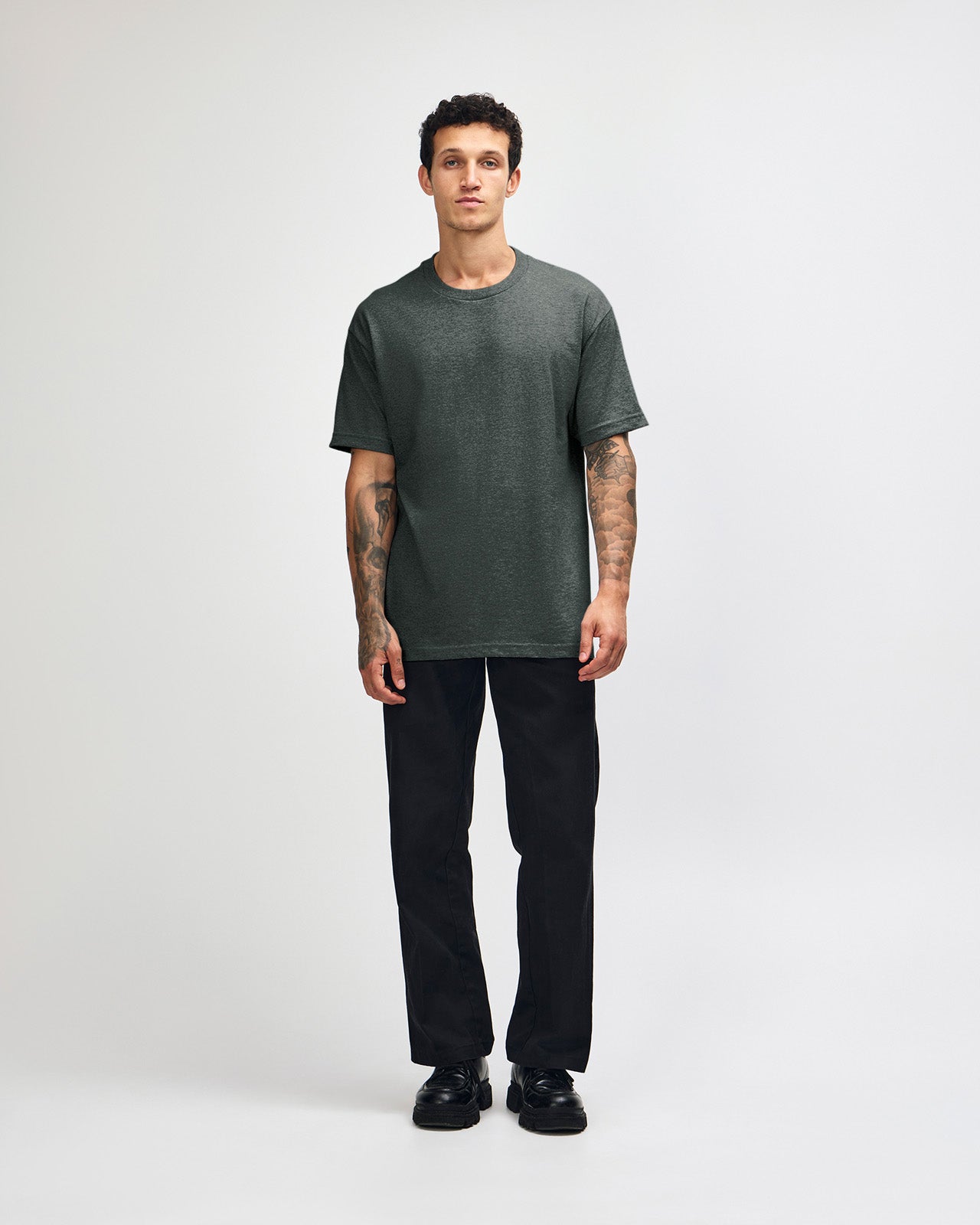 Male Model wearing a Heather Charcoal Heavyweight Unisex Short Sleeve Crew Neck Tee, paired with blue jeans, standing against a plain background (front pose) -heather charcoal