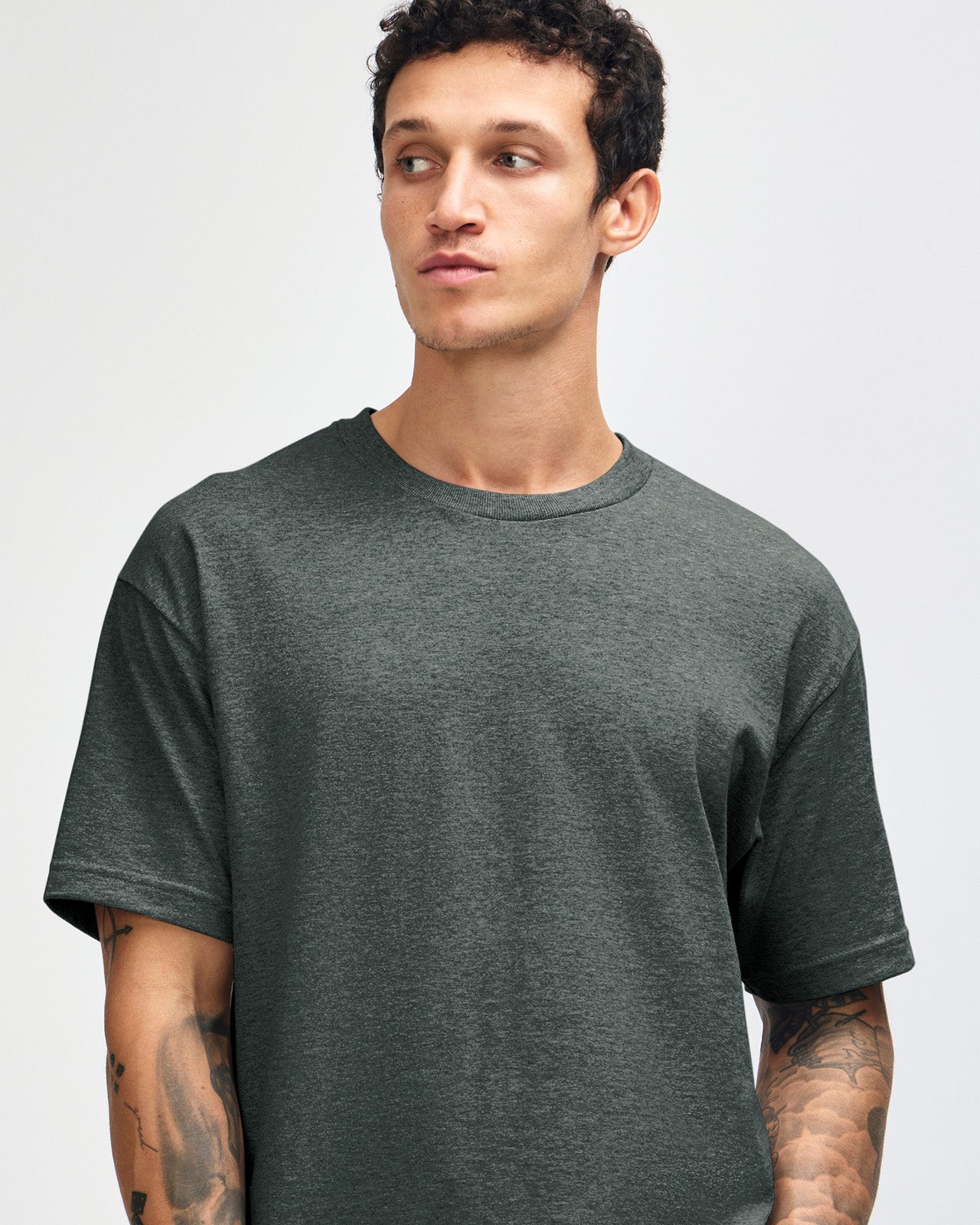 Male Model wearing a Heather Charcoal Heavyweight Unisex Short Sleeve Crew Neck Tee, paired with blue jeans, standing against a plain background (front pose) -heather charcoal