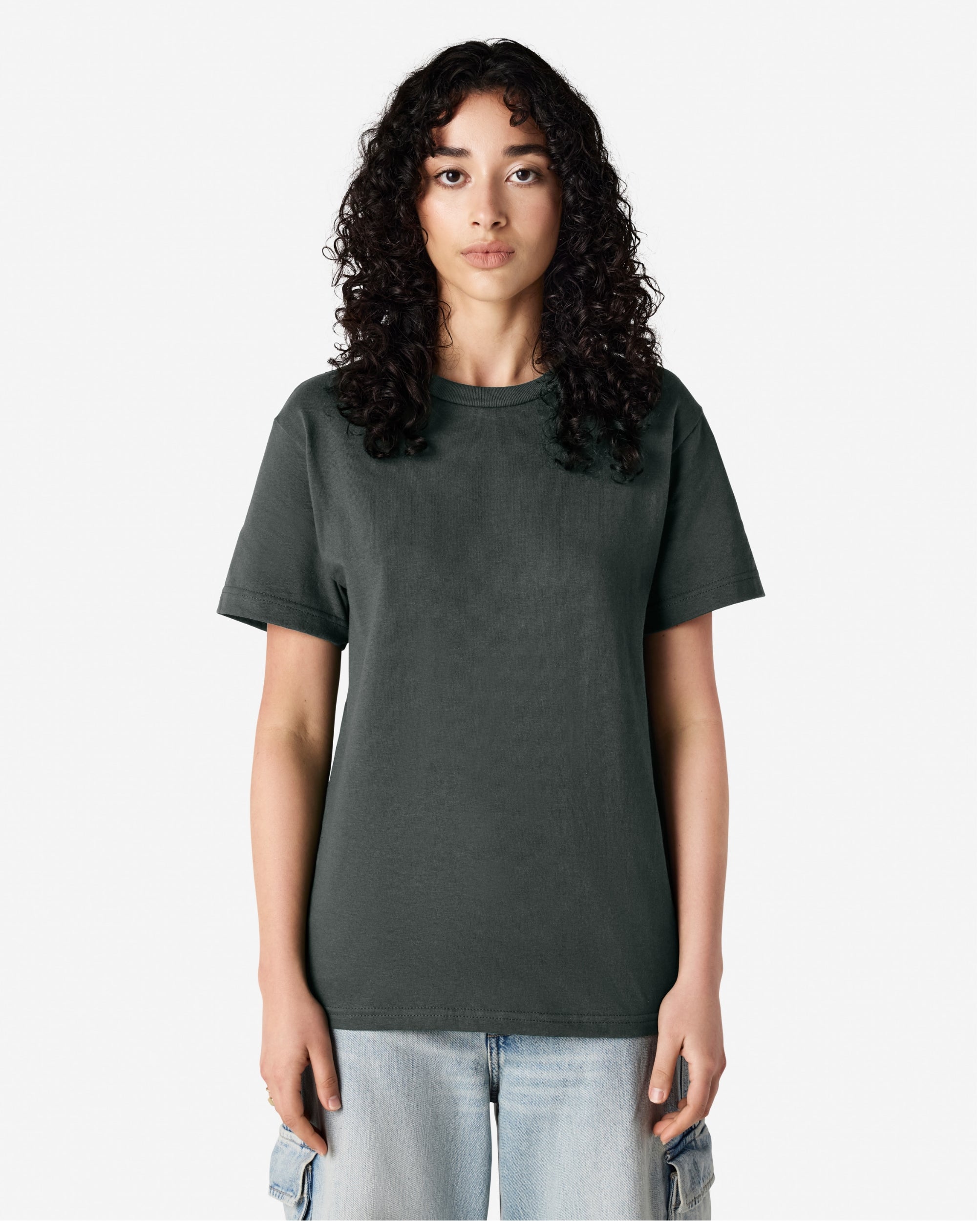 female Model wearing a Heather Charcoal Heavyweight Unisex Short Sleeve Crew Neck Tee, paired with blue jeans, standing against a plain background (front pose) -heather charcoal