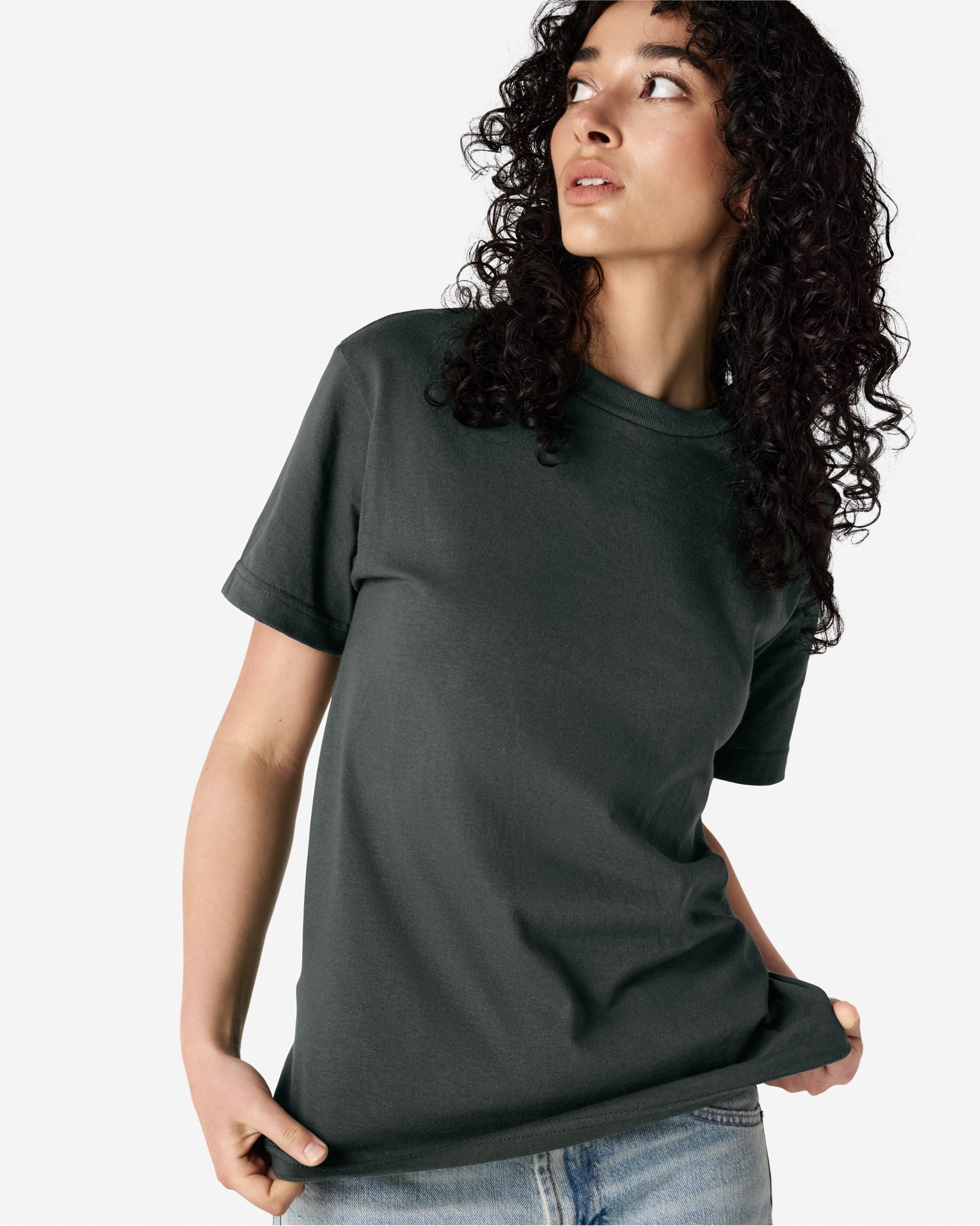 Female Model wearing a Heather Charcoal Heavyweight Unisex Short Sleeve Crew Neck Tee, paired with blue jeans, standing against a plain background (front pose) -heather charcoal