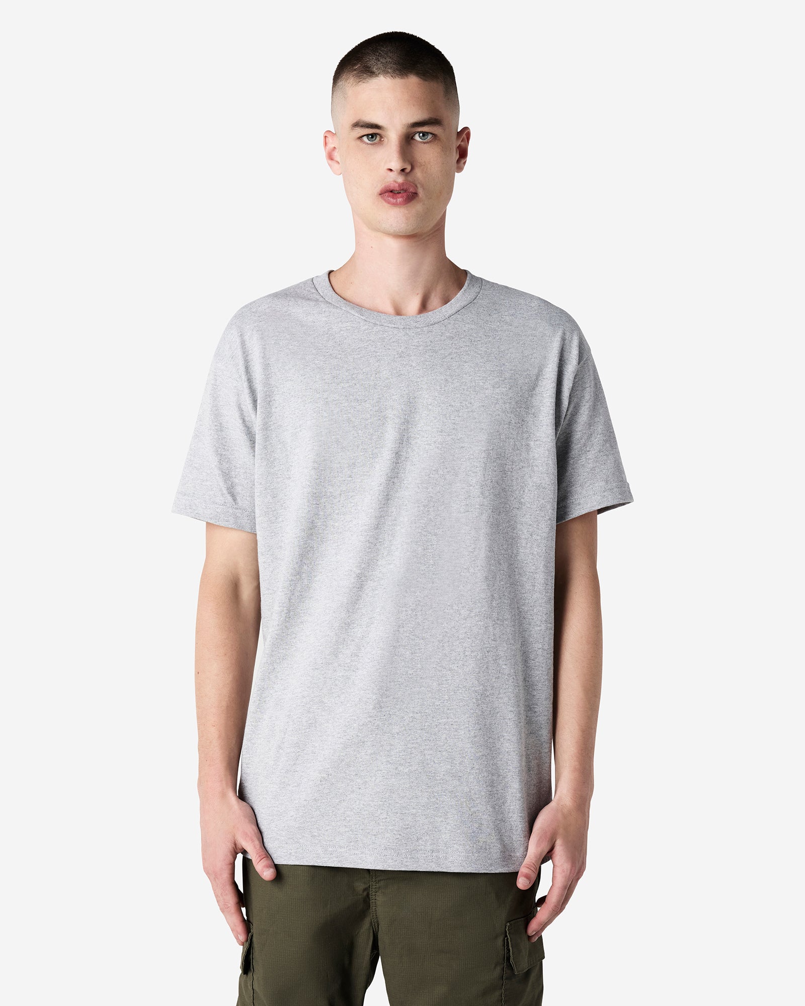 Male Model wearing a Heather Grey Heavyweight Unisex Short Sleeve Crew Neck Tee, paired with blue jeans, standing against a plain background (front pose) -heather grey
