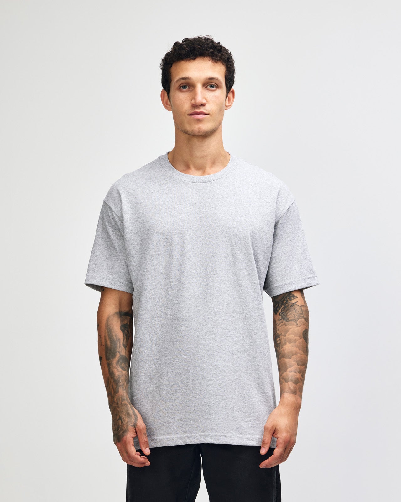 Male Model wearing a Heather Grey Heavyweight Unisex Short Sleeve Crew Neck Tee, paired with blue jeans, standing against a plain background (front pose) -heather grey