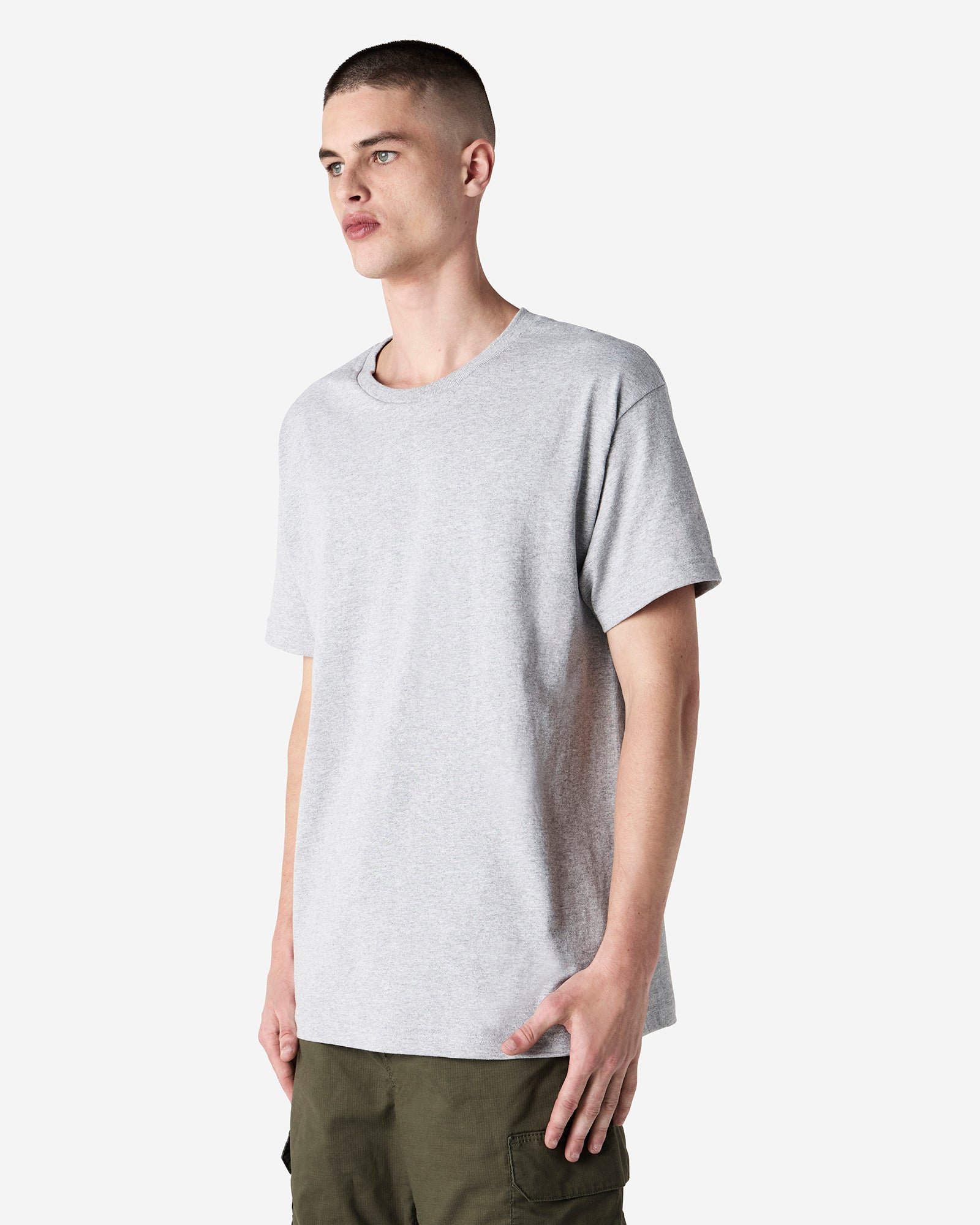 Male Model wearing a Heather Grey Heavyweight Unisex Short Sleeve Crew Neck Tee, paired with blue jeans, standing against a plain background (front pose) -heather grey