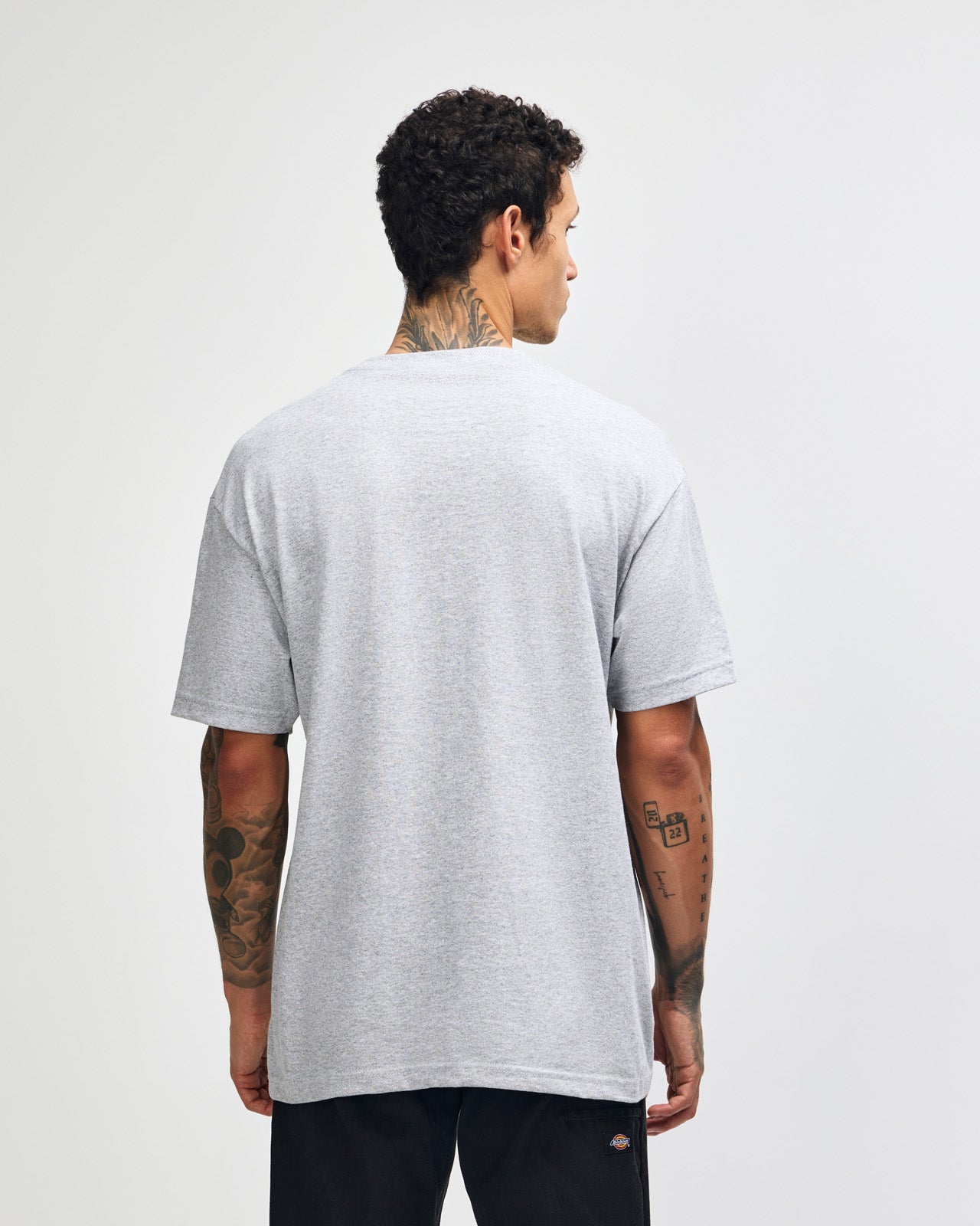 Male Model wearing a Heather Grey Heavyweight Unisex Short Sleeve Crew Neck Tee, paired with blue jeans, standing against a plain background (front pose) -heather grey