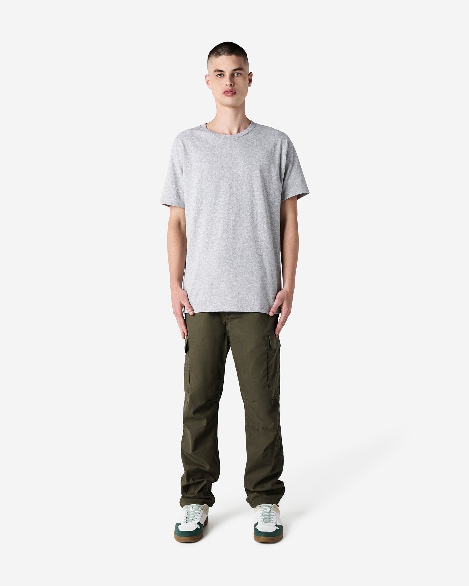 Male Model wearing a HeatherGrey Heavyweight Unisex Short Sleeve Crew Neck Tee, paired with green jeans, standing against a plain background (front pose) -heather grey