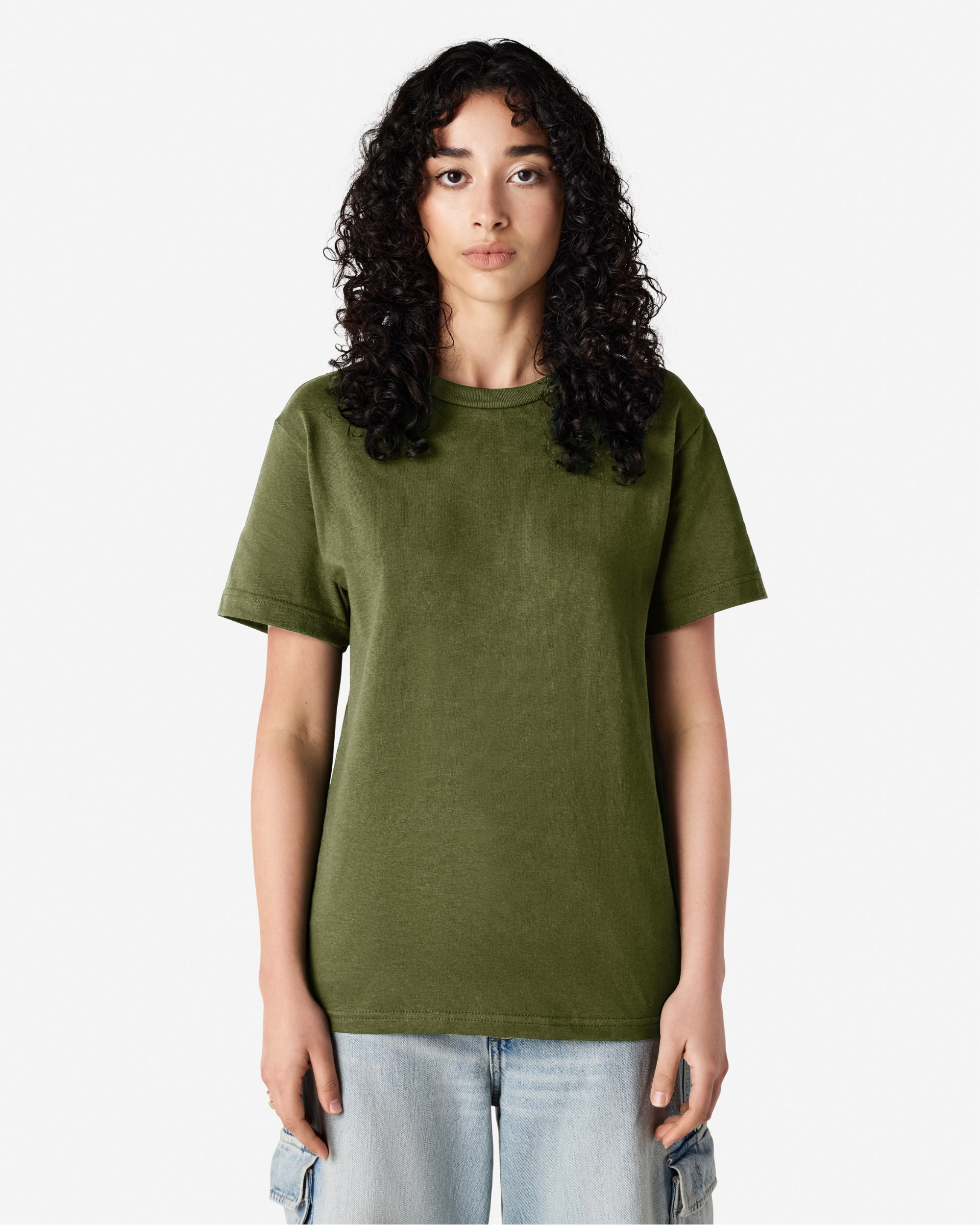 Female Model wearing a Military Green Heavyweight Unisex Short Sleeve Crew Neck Tee, paired with blue jeans, standing against a plain background (front pose) -military green