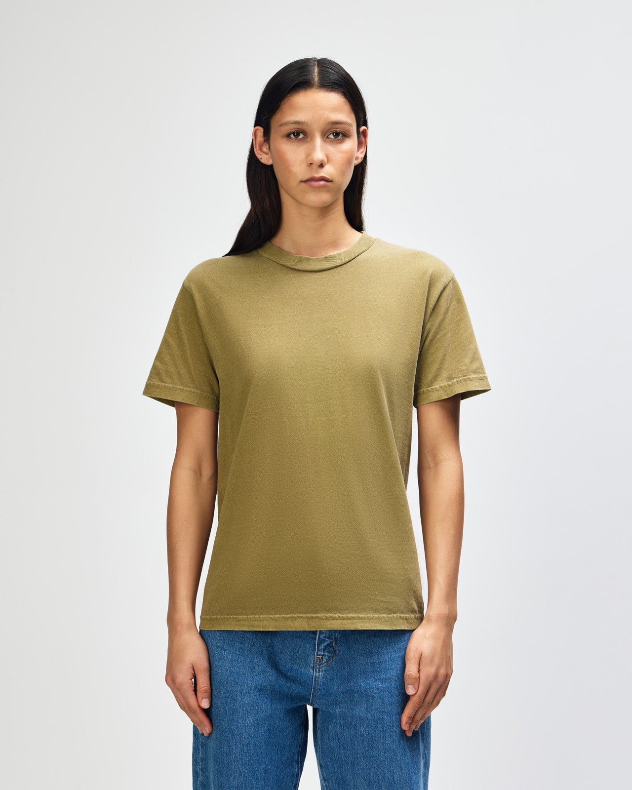 Female Model wearing a Military Green Heavyweight Unisex Short Sleeve Crew Neck Tee, paired with blue jeans, standing against a plain background (front pose) -military green