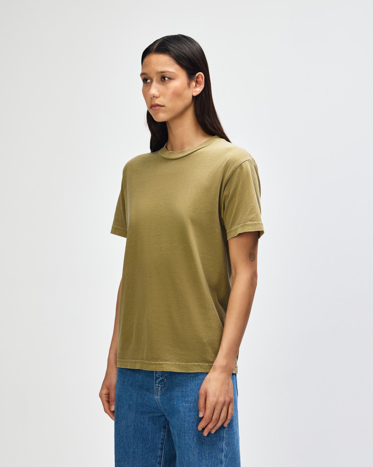Female Model wearing a Military Green Heavyweight Unisex Short Sleeve Crew Neck Tee, paired with blue jeans, standing against a plain background (front pose) -military green