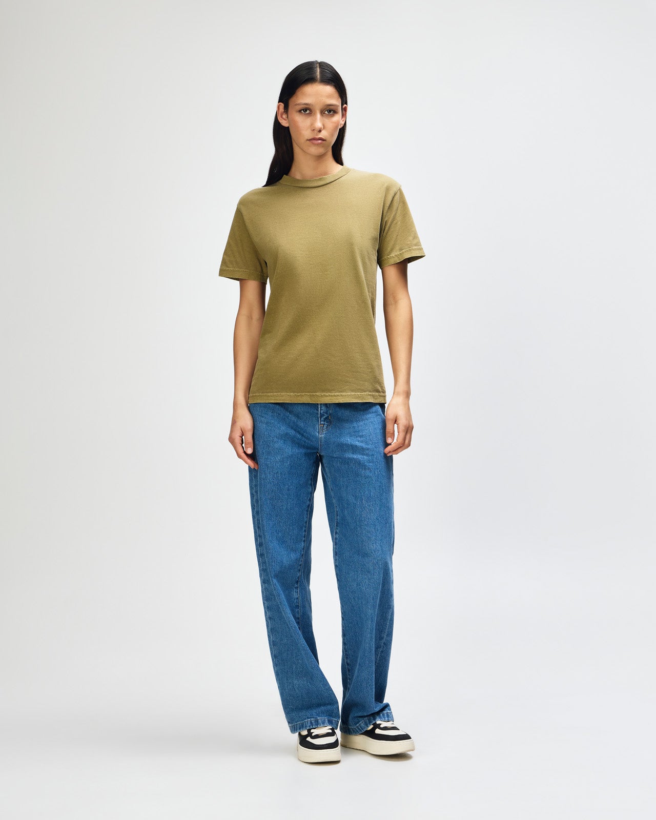 Female Model wearing a Military Green Heavyweight Unisex Short Sleeve Crew Neck Tee, paired with blue jeans, standing against a plain background (front pose) -military green