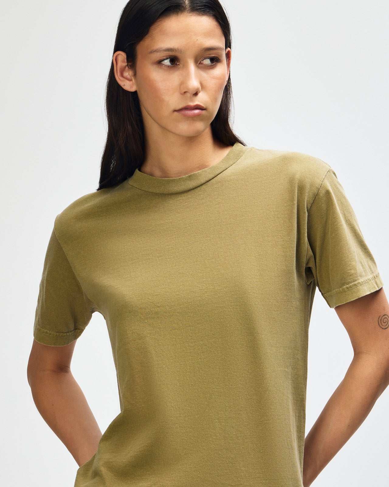 Female Model wearing a Military Green Heavyweight Unisex Short Sleeve Crew Neck Tee, paired with blue jeans, standing against a plain background (front pose) -military green