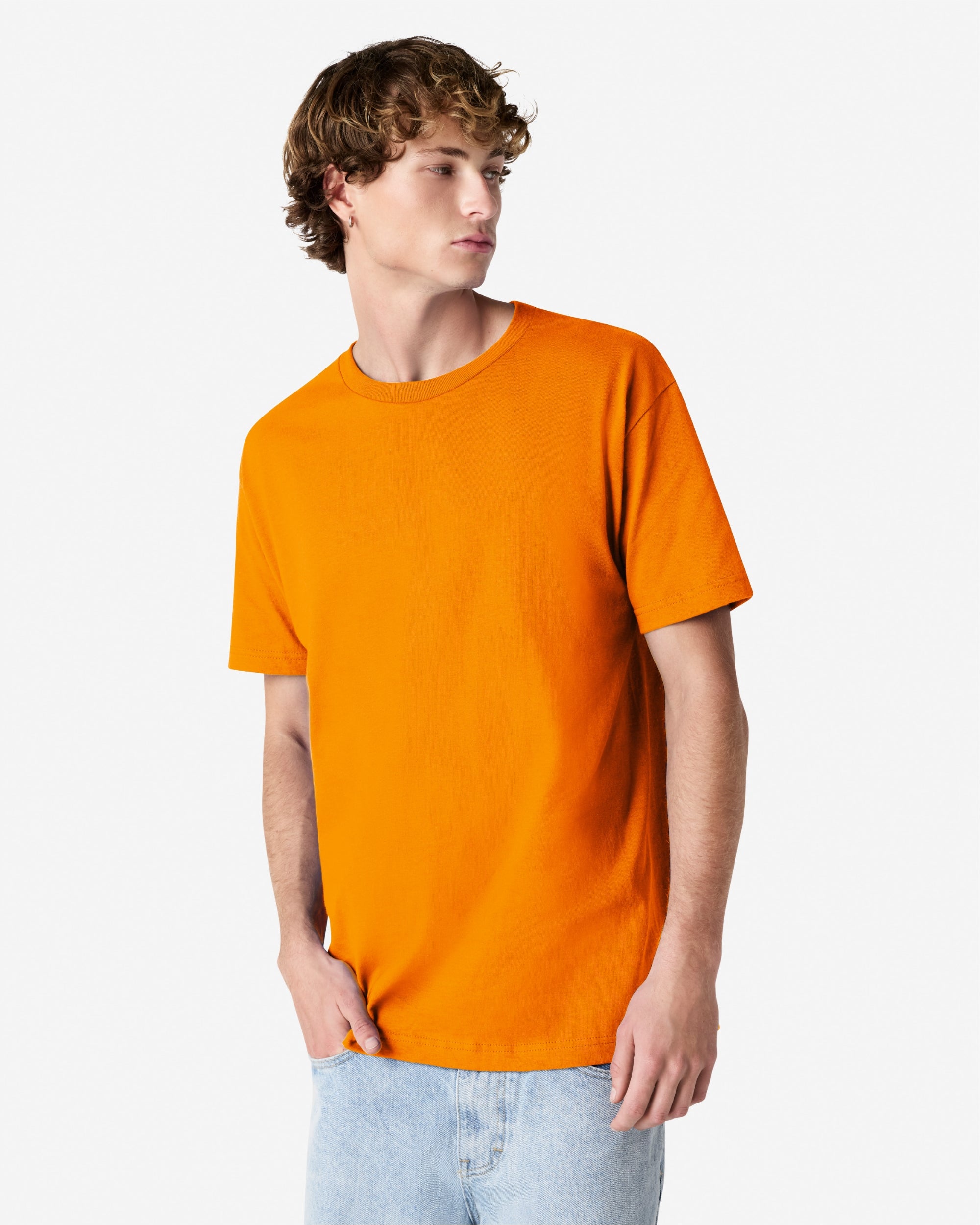 Male Model wearing a Pink Heavyweight Unisex Short Sleeve Crew Neck Tee, paired with blue jeans, standing against a plain background (front pose) -orange