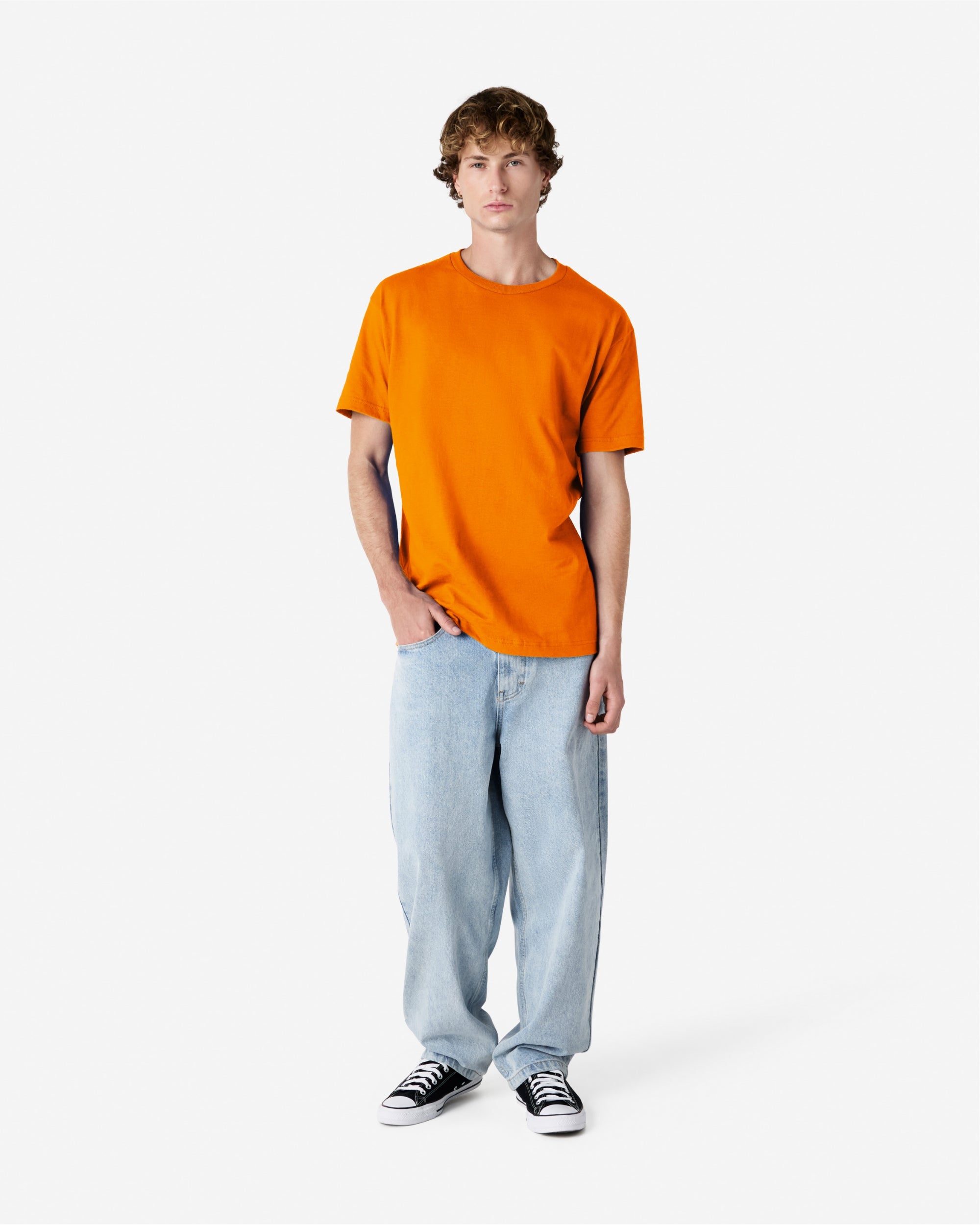 Male Model wearing a Orange Heavyweight Unisex Short Sleeve Crew Neck Tee, paired with blue jeans, standing against a plain background (front pose) -orange