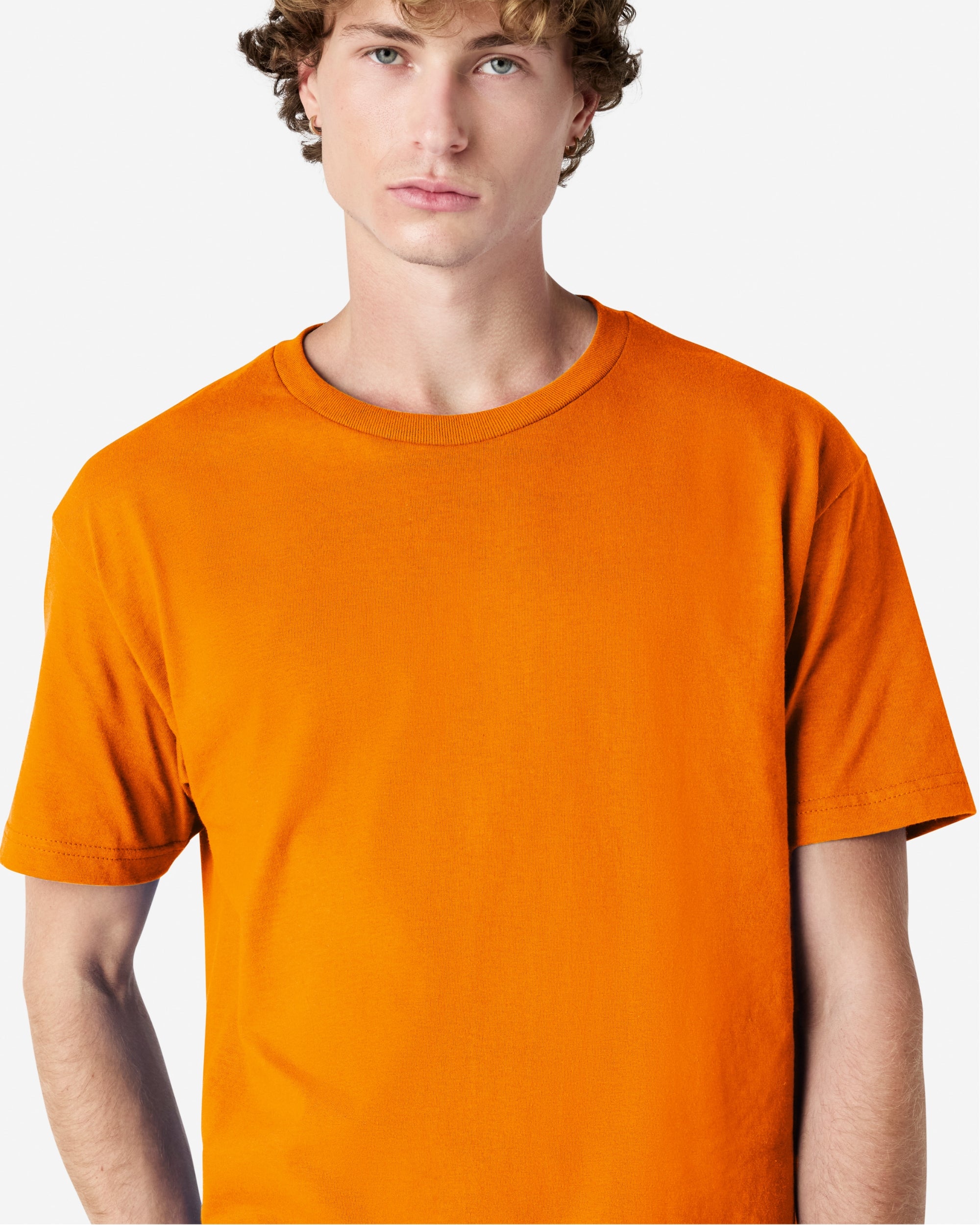 Male Model wearing a Orange Heavyweight Unisex Short Sleeve Crew Neck Tee, paired with blue jeans, standing against a plain background (front pose) -orange