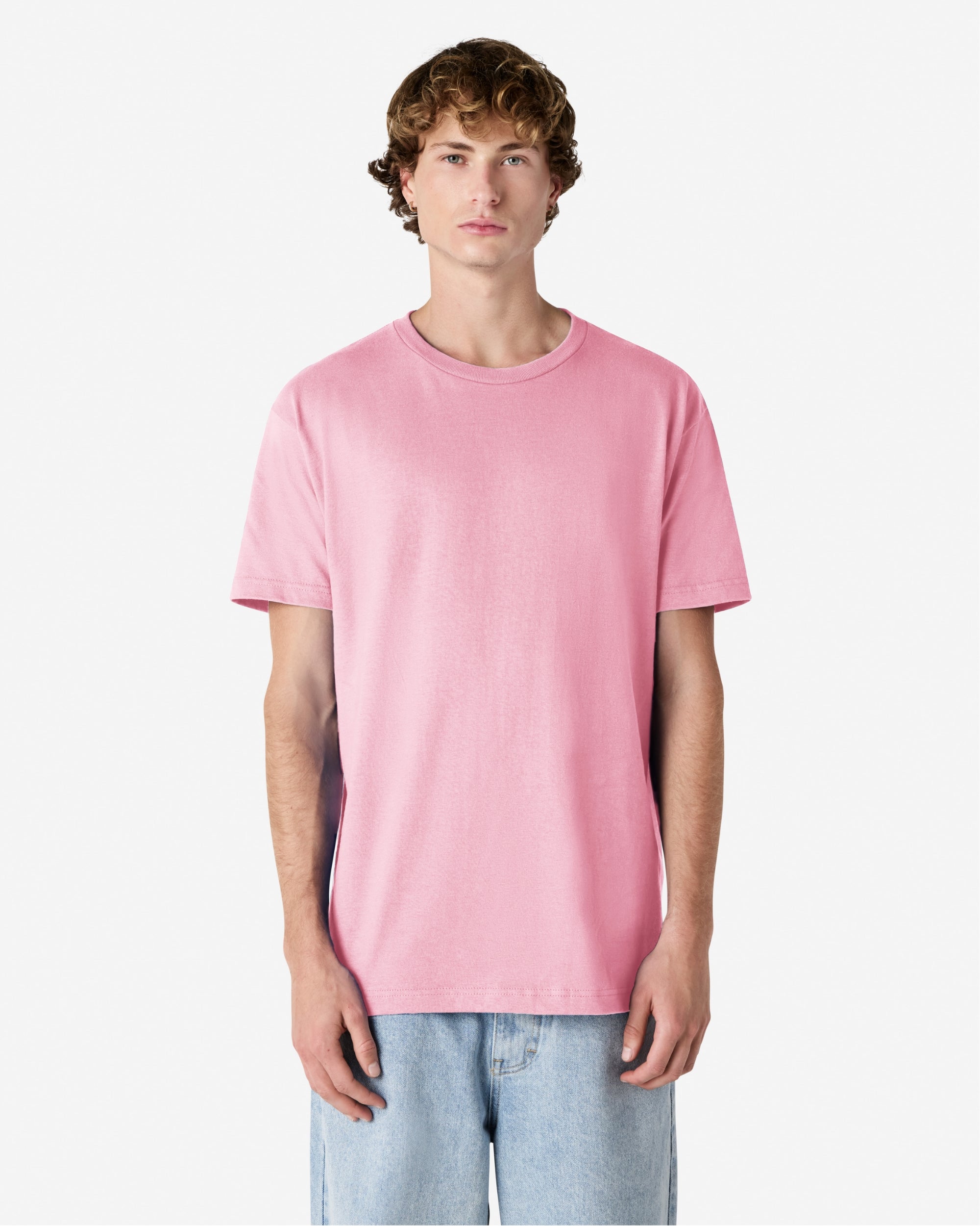 Male Model wearing a pink Heavyweight Unisex Short Sleeve Crew Neck Tee, paired with blue jeans, standing against a plain background (front pose) -pink
