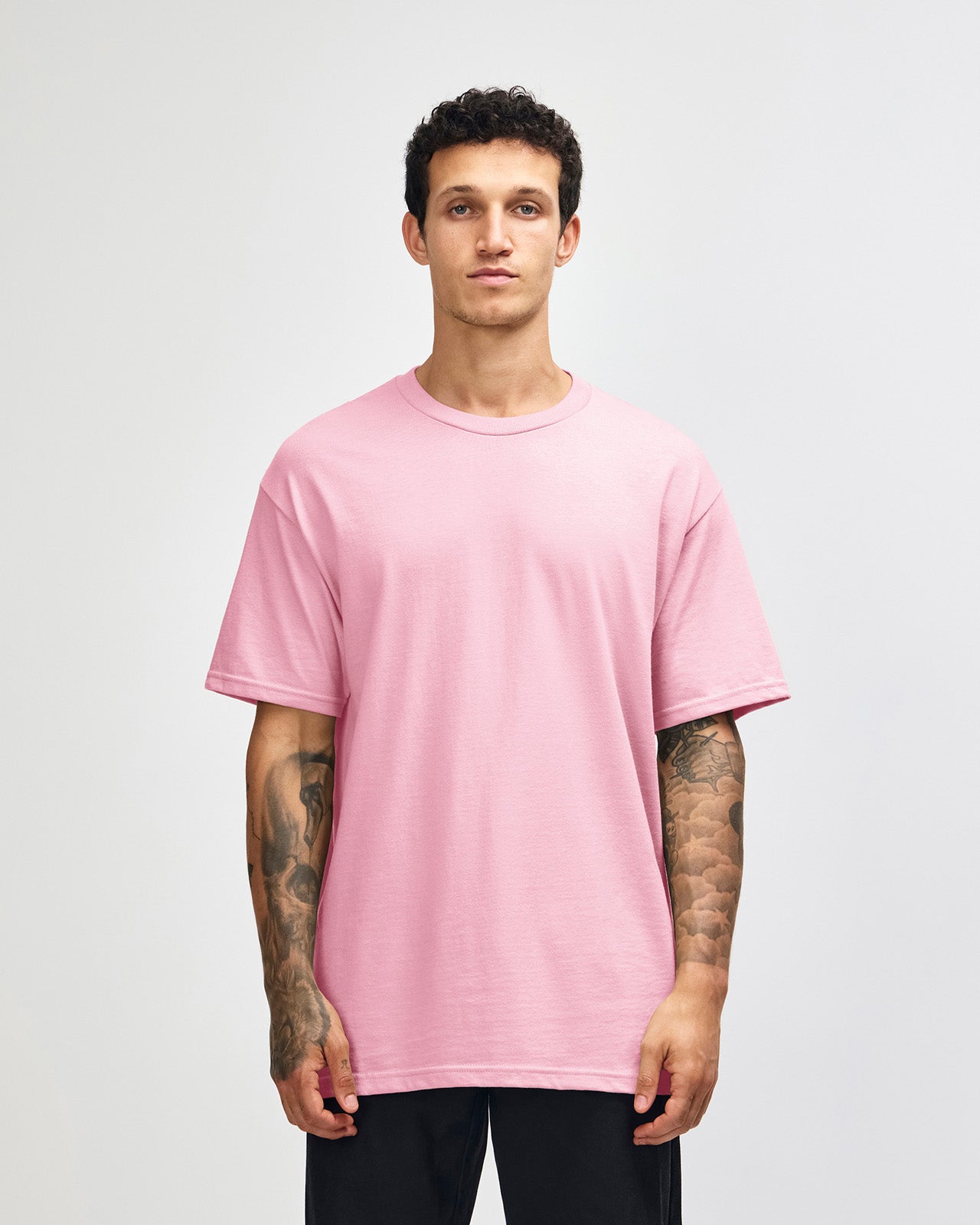 Male Model wearing a pink Heavyweight Unisex Short Sleeve Crew Neck Tee, paired with blue jeans, standing against a plain background (front pose) -pink