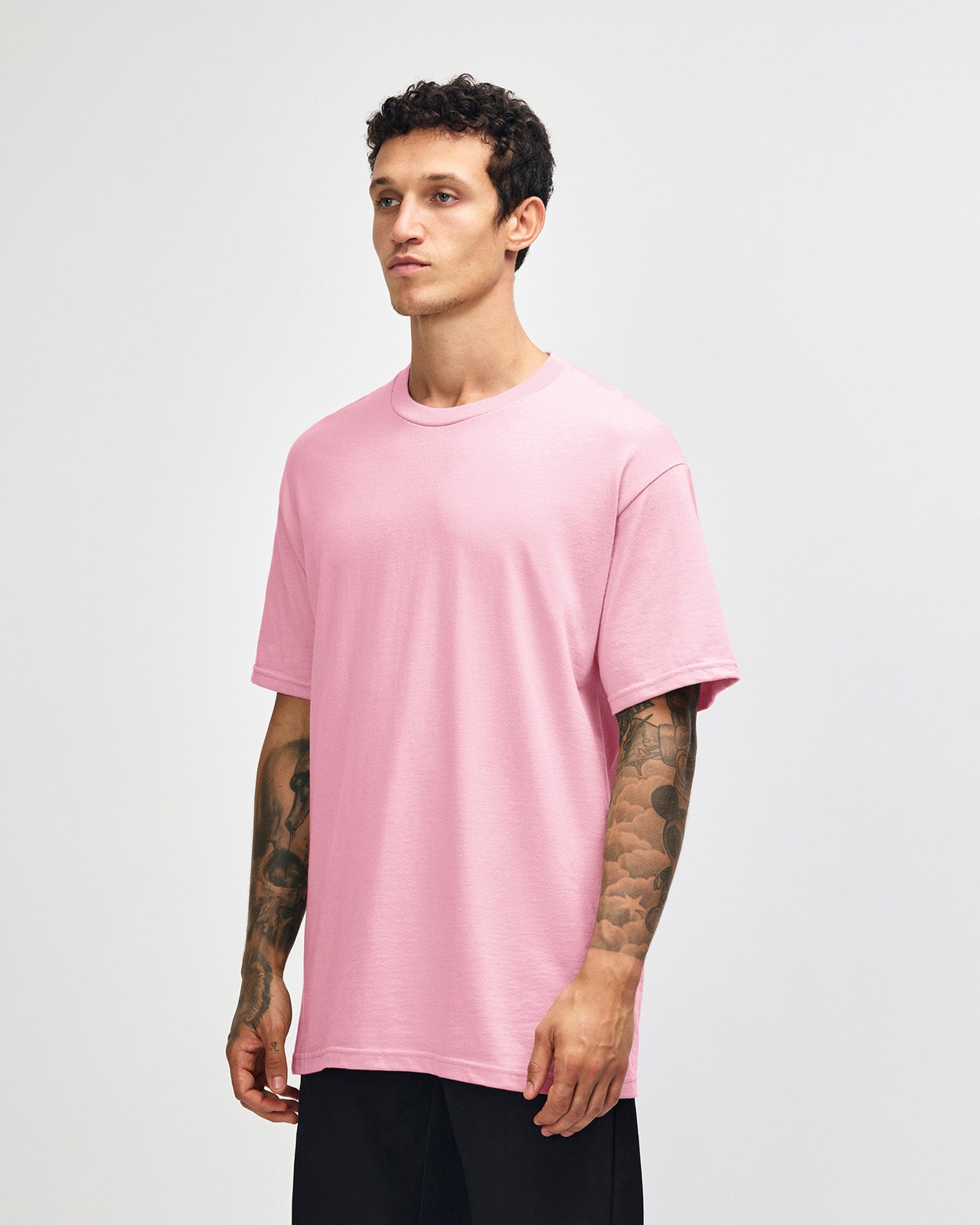 Male Model wearing a pink Heavyweight Unisex Short Sleeve Crew Neck Tee, paired with blue jeans, standing against a plain background (front pose) -pink