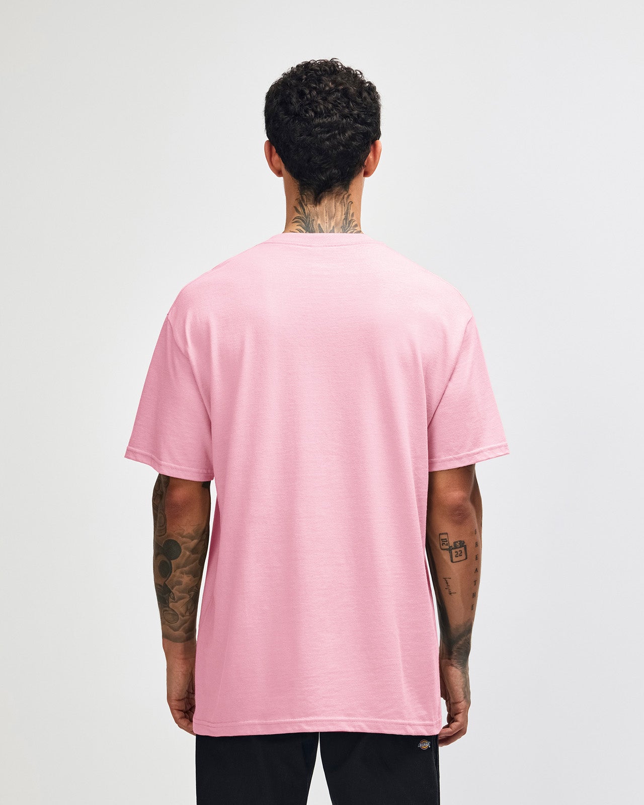 Male Model wearing a pink Heavyweight Unisex Short Sleeve Crew Neck Tee, paired with blue jeans, standing against a plain background (front pose) -pink