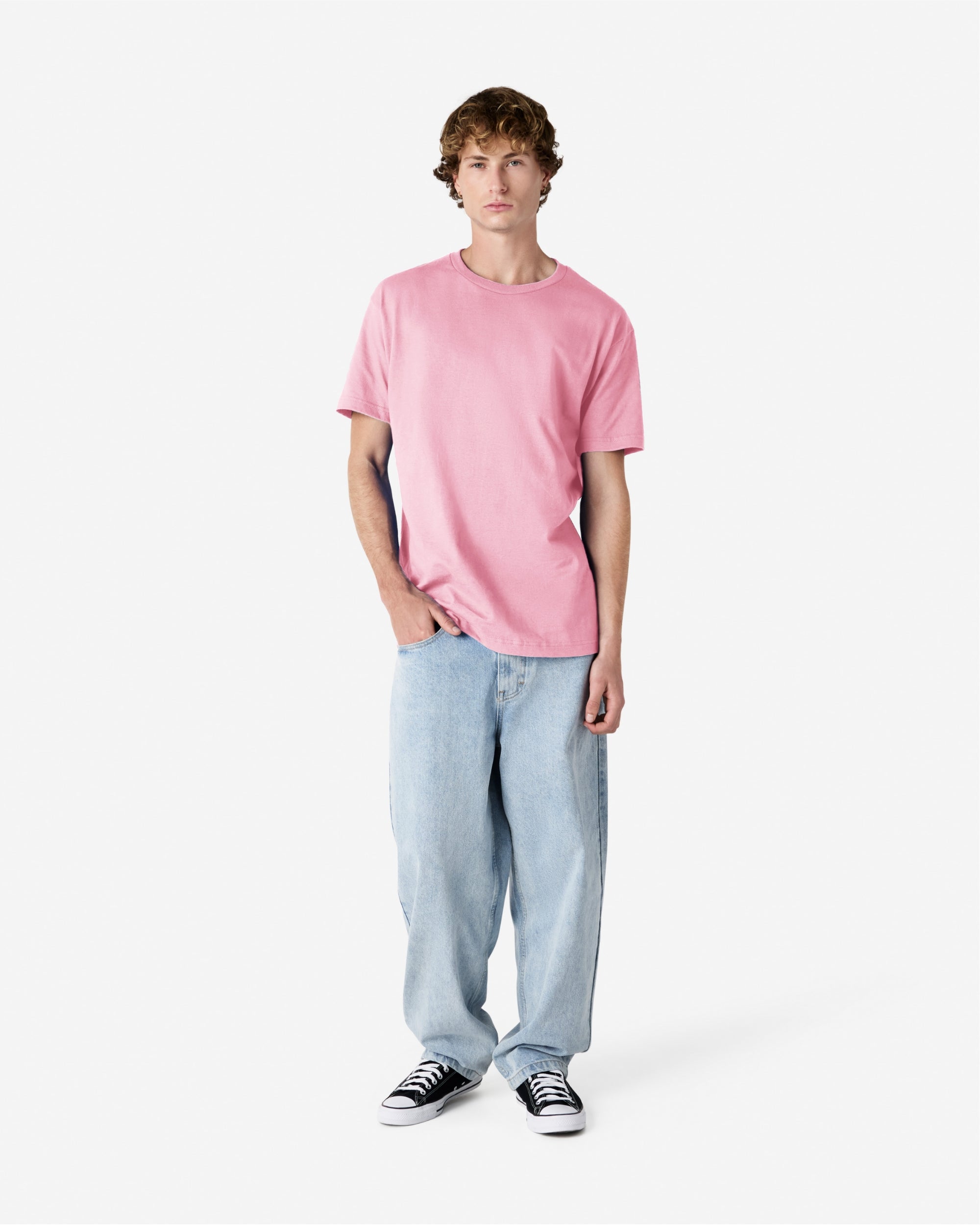 Male Model wearing a Pink Heavyweight Unisex Short Sleeve Crew Neck Tee, paired with blue jeans, standing against a plain background (front pose) -pink
