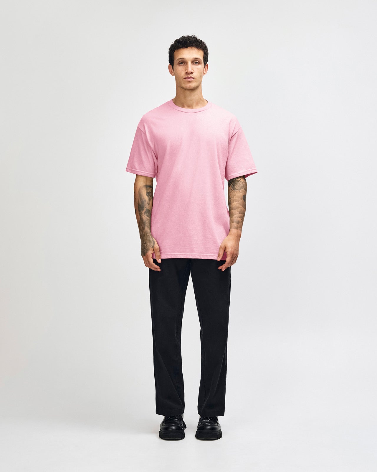 Male Model wearing a pink Heavyweight Unisex Short Sleeve Crew Neck Tee, paired with blue jeans, standing against a plain background (front pose) -pink