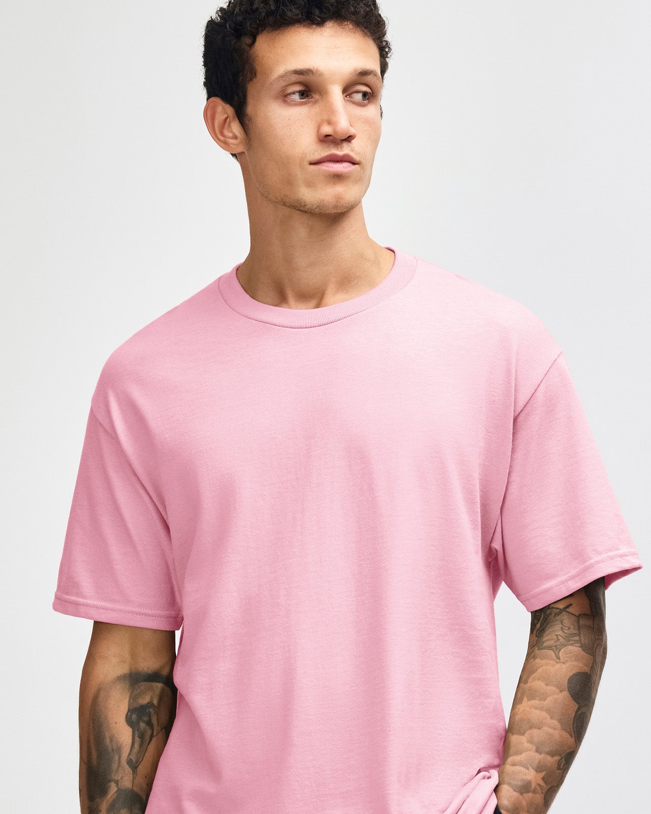 Male Model wearing a pink Heavyweight Unisex Short Sleeve Crew Neck Tee, paired with blue jeans, standing against a plain background (front pose) -pink