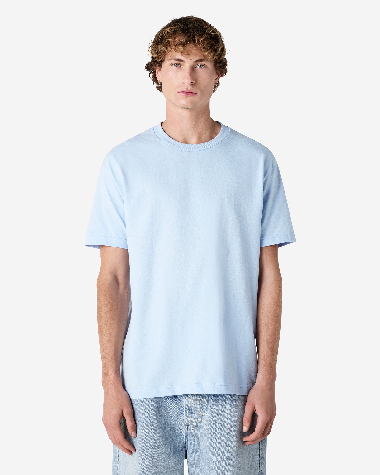 Male Model wearing a Powder Blue Heavyweight Unisex Short Sleeve Crew Neck Tee, paired with blue jeans, standing against a plain background (front pose) -powder blue