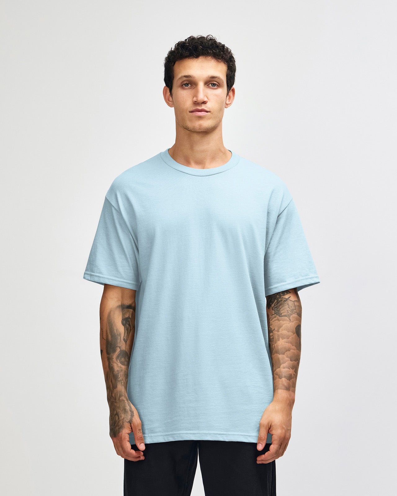 Male Model wearing a Powder Blue Heavyweight Unisex Short Sleeve Crew Neck Tee, paired with blue jeans, standing against a plain background (front pose) -powder blue