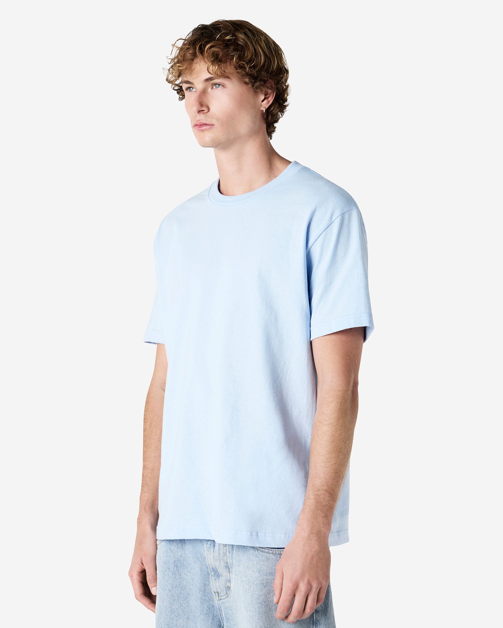 Male Model wearing a Powder Blue Heavyweight Unisex Short Sleeve Crew Neck Tee, paired with blue jeans, standing against a plain background (front pose) -powder blue
