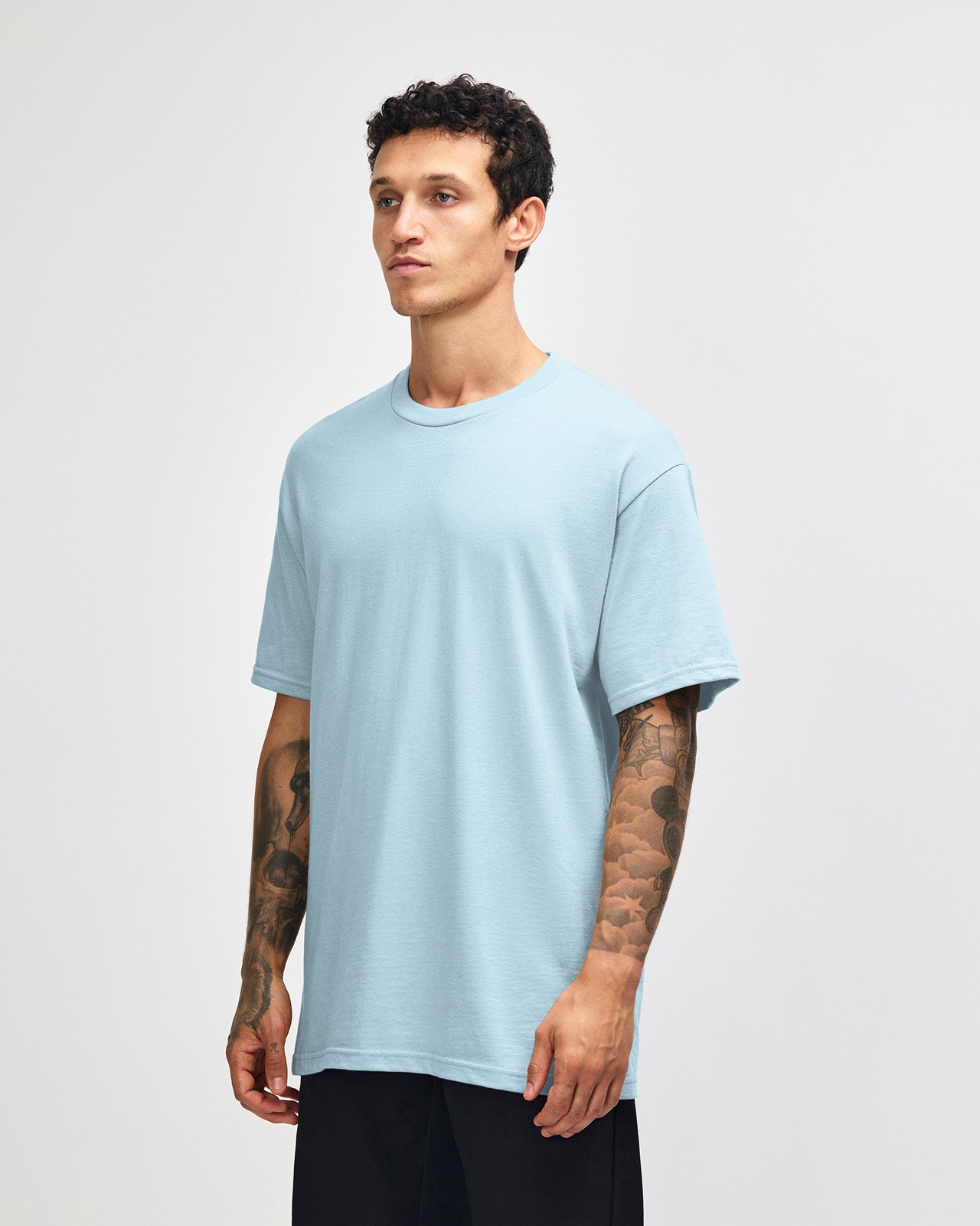 Male Model wearing a Powder Blue Heavyweight Unisex Short Sleeve Crew Neck Tee, paired with blue jeans, standing against a plain background (front pose) -powder blue