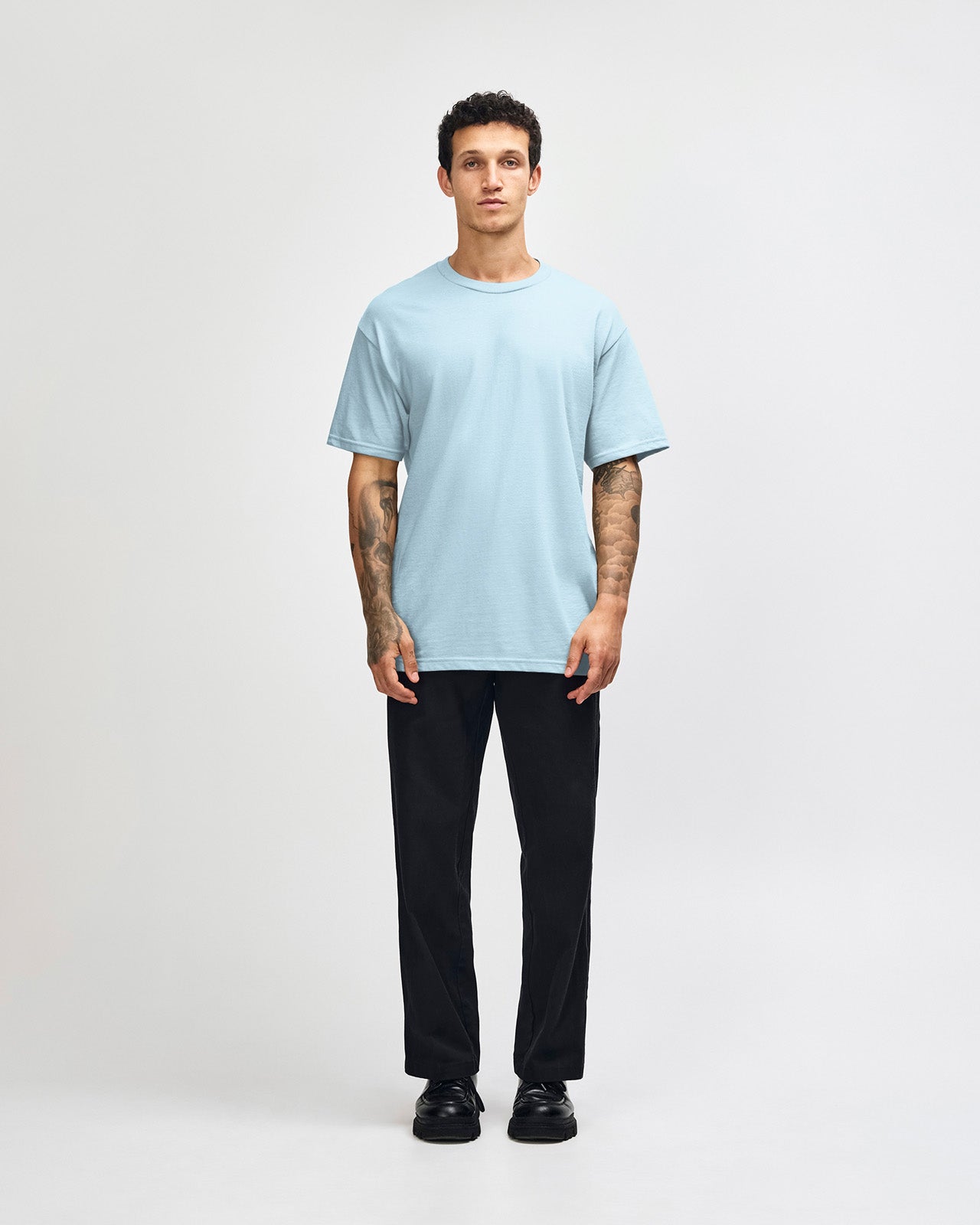 Male Model wearing a Powder Blue Heavyweight Unisex Short Sleeve Crew Neck Tee, paired with blue jeans, standing against a plain background (front pose) -powder blue