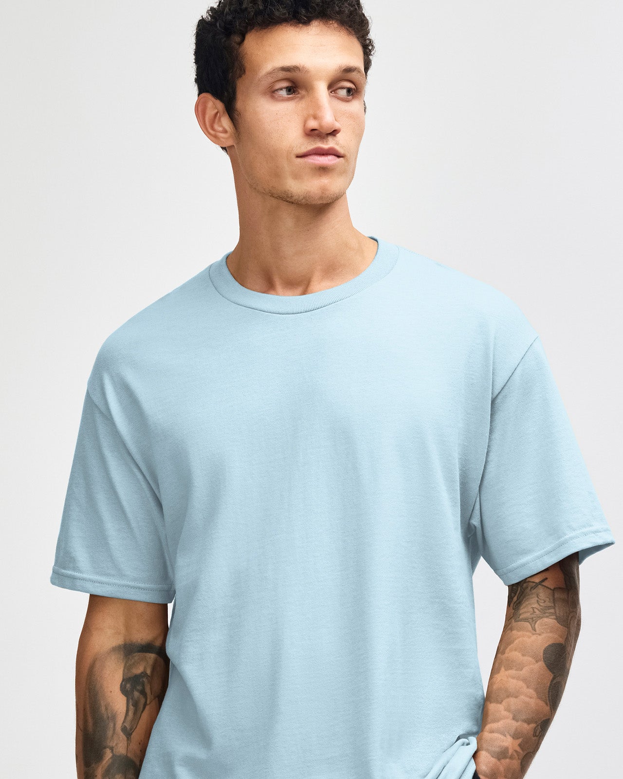 Male Model wearing a Powder Blue Heavyweight Unisex Short Sleeve Crew Neck Tee, paired with blue jeans, standing against a plain background (front pose) -powder blue