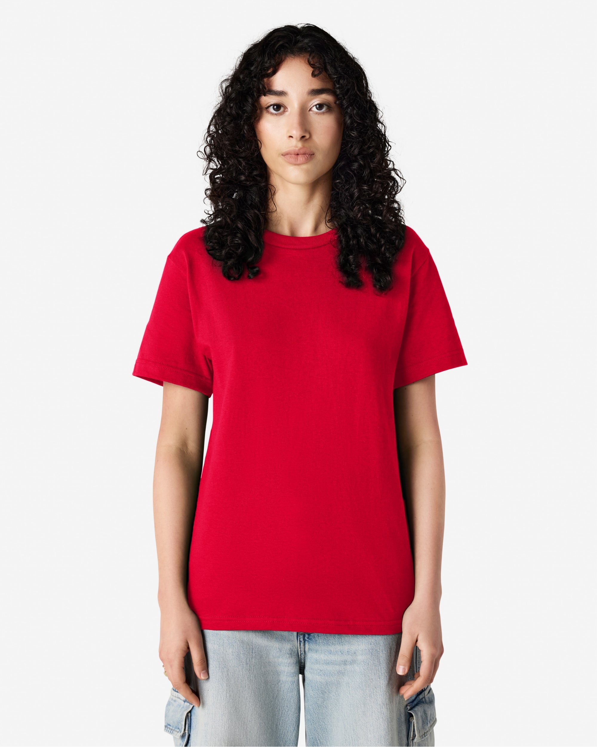 Female Model wearing a red Heavyweight Unisex Short Sleeve Crew Neck Tee, paired with blue jeans, standing against a plain background (front pose) -red