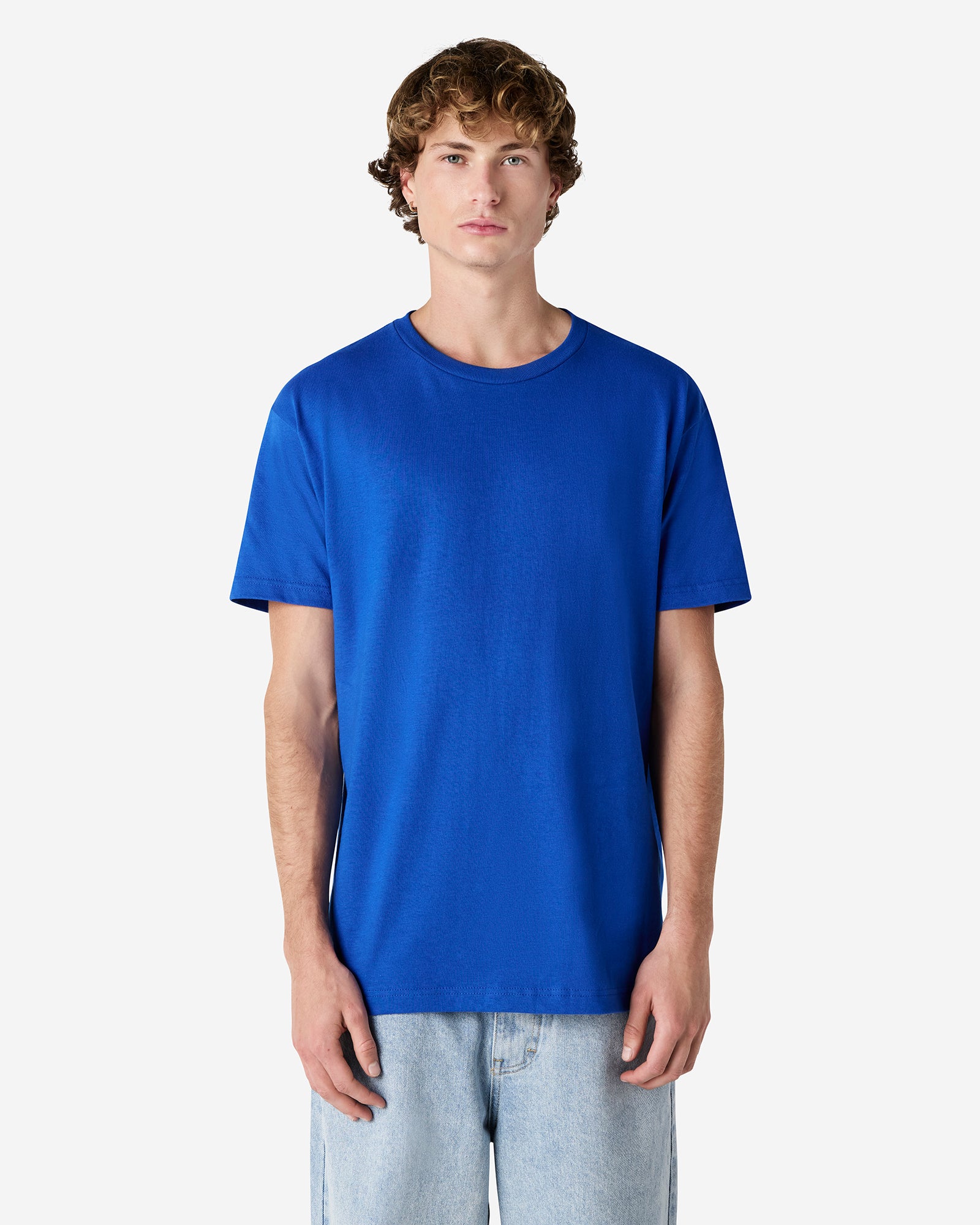 Male Model wearing a Royal Heavyweight Unisex Short Sleeve Crew Neck Tee, paired with blue jeans, standing against a plain background (front pose) -royal