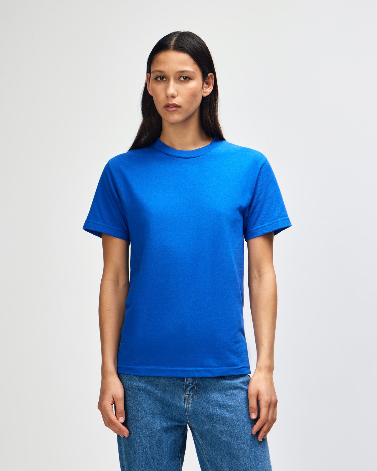 Female Model wearing a red Heavyweight Unisex Short Sleeve Crew Neck Tee, paired with blue jeans, standing against a plain background (front pose) -royal